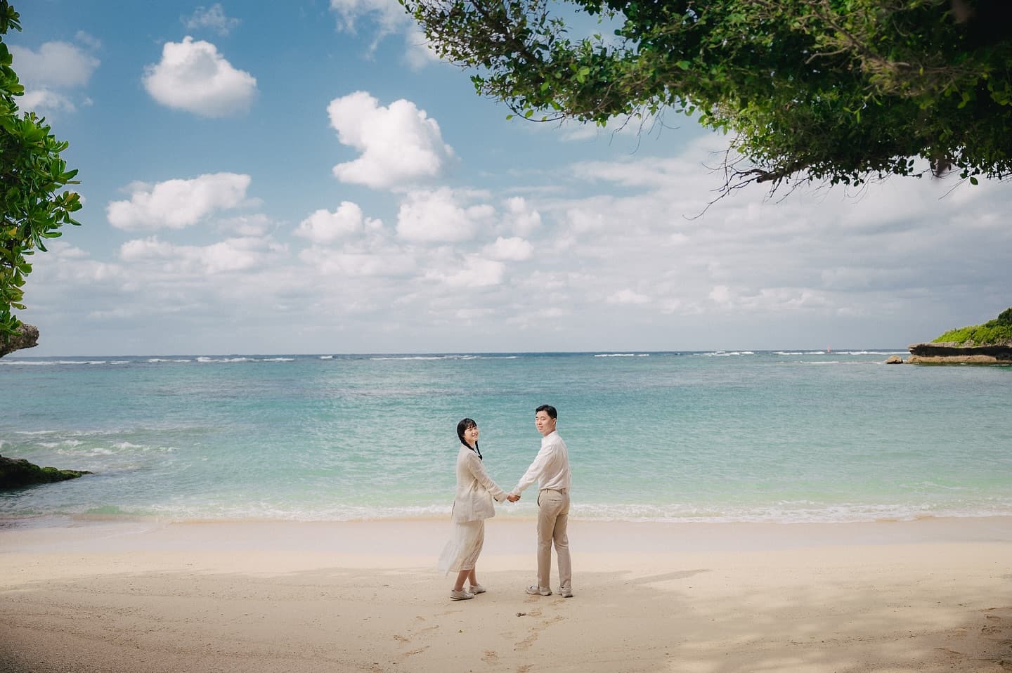 Couple holding hands on a secluded cove beach with turquoise sea in Okinawa