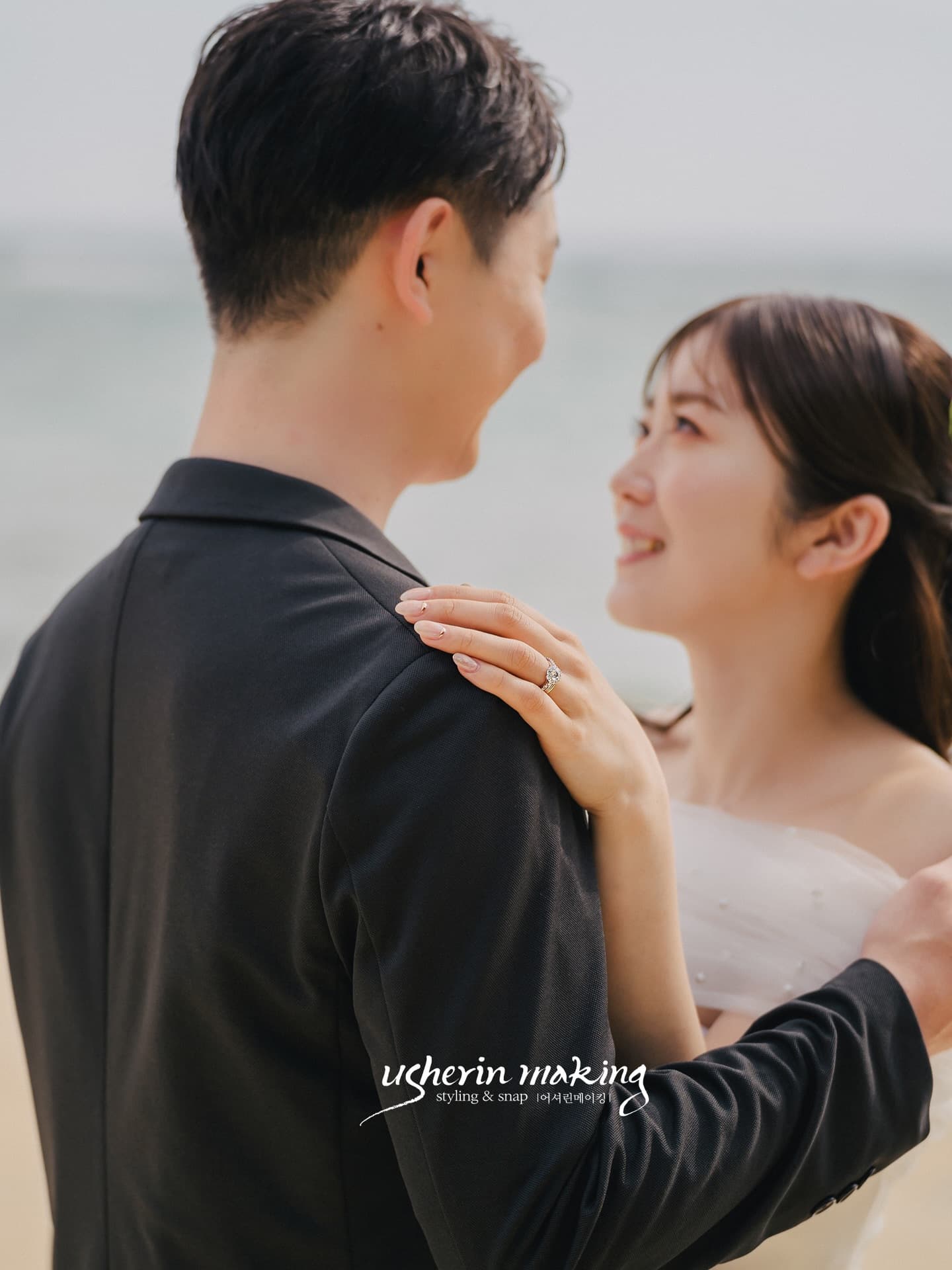 바닷가에서 신랑을 올려다보며 웃는 신부, 어깨에 얹은 손의 반지 클로즈업