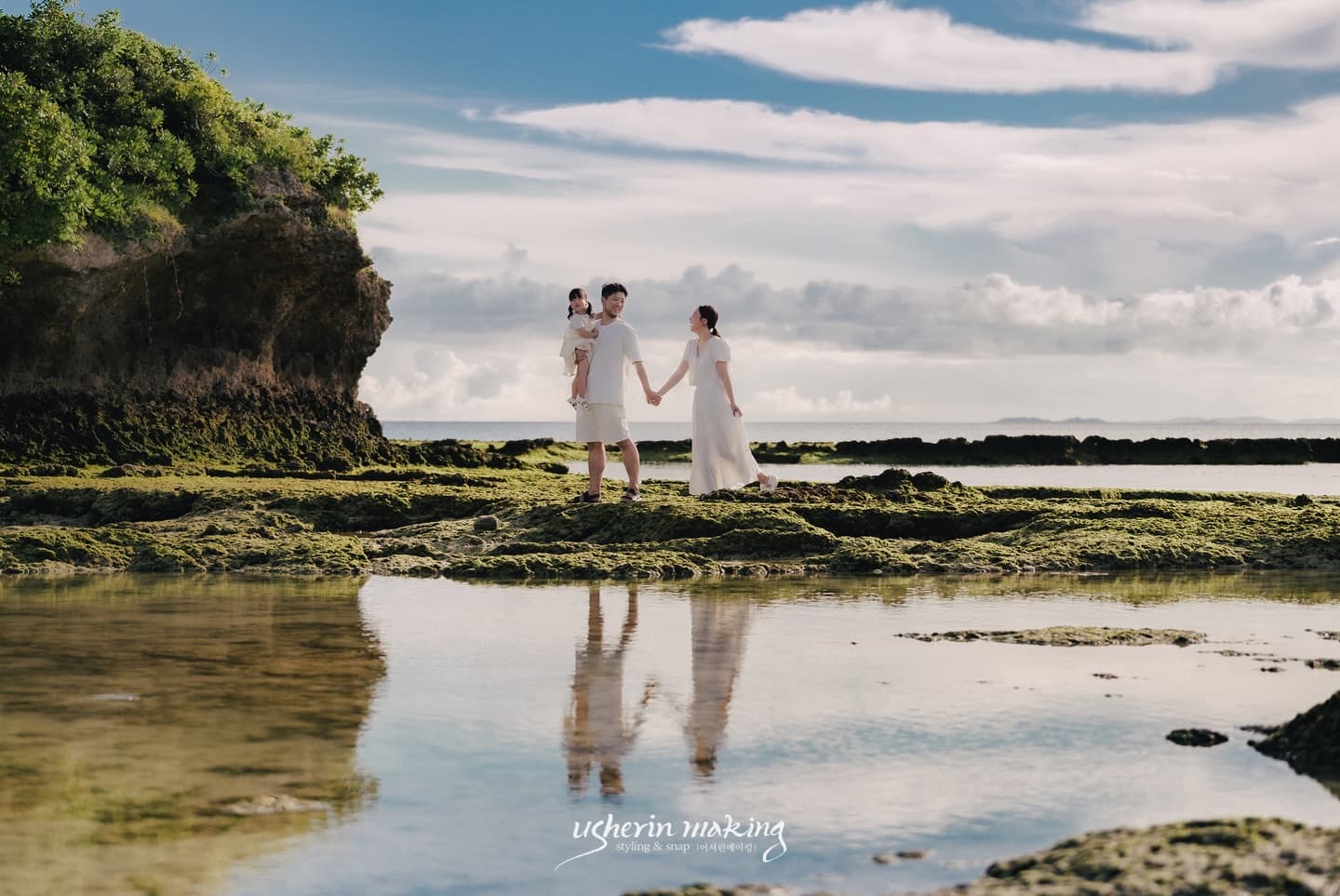 Family walking hand in hand across mossy tide pools that mirror them, Okinawa on a clear day