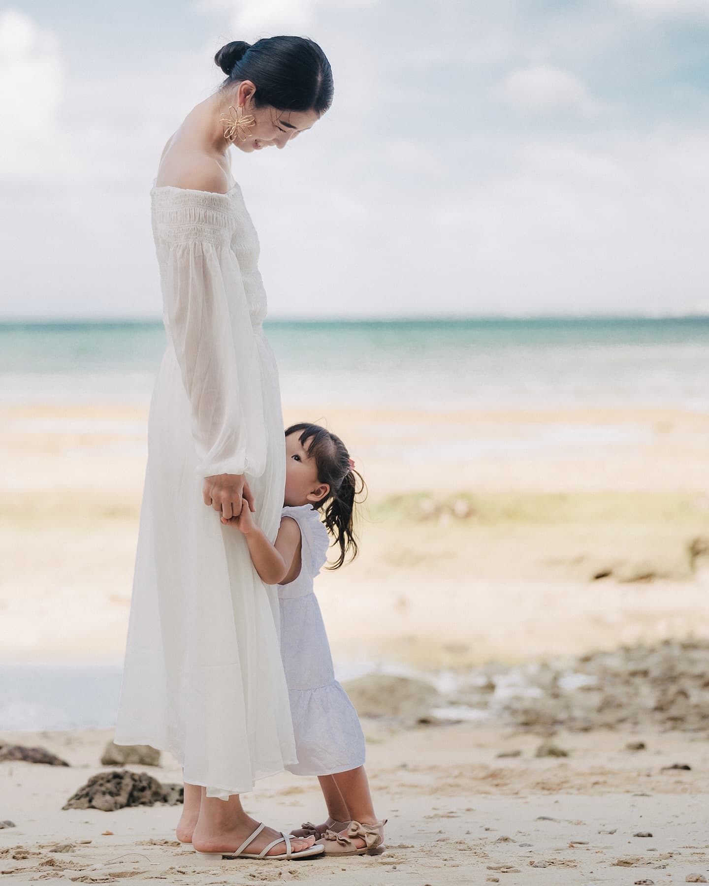 Little girl hugging her mother's legs on a cloudy Okinawa beach