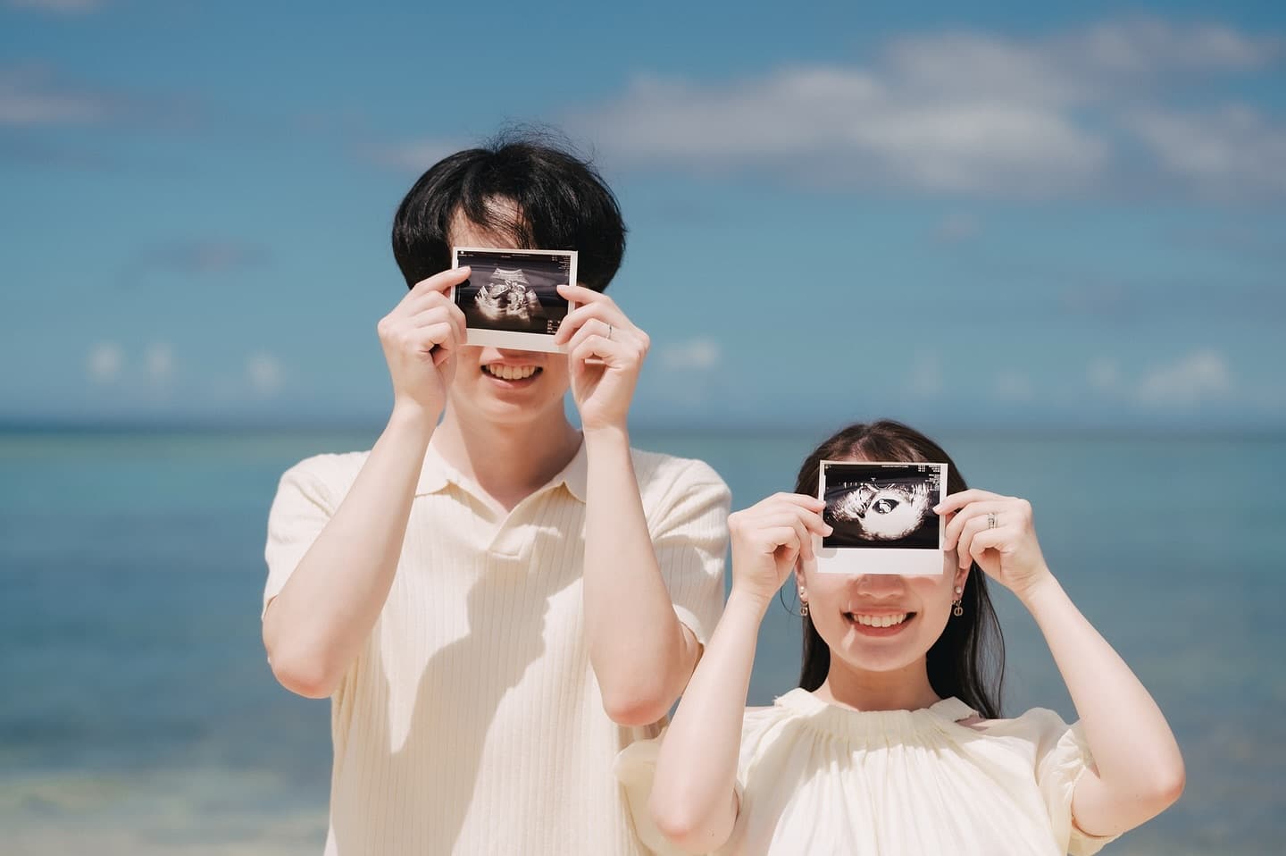Smiling parents-to-be holding ultrasound photos on an Okinawa beach