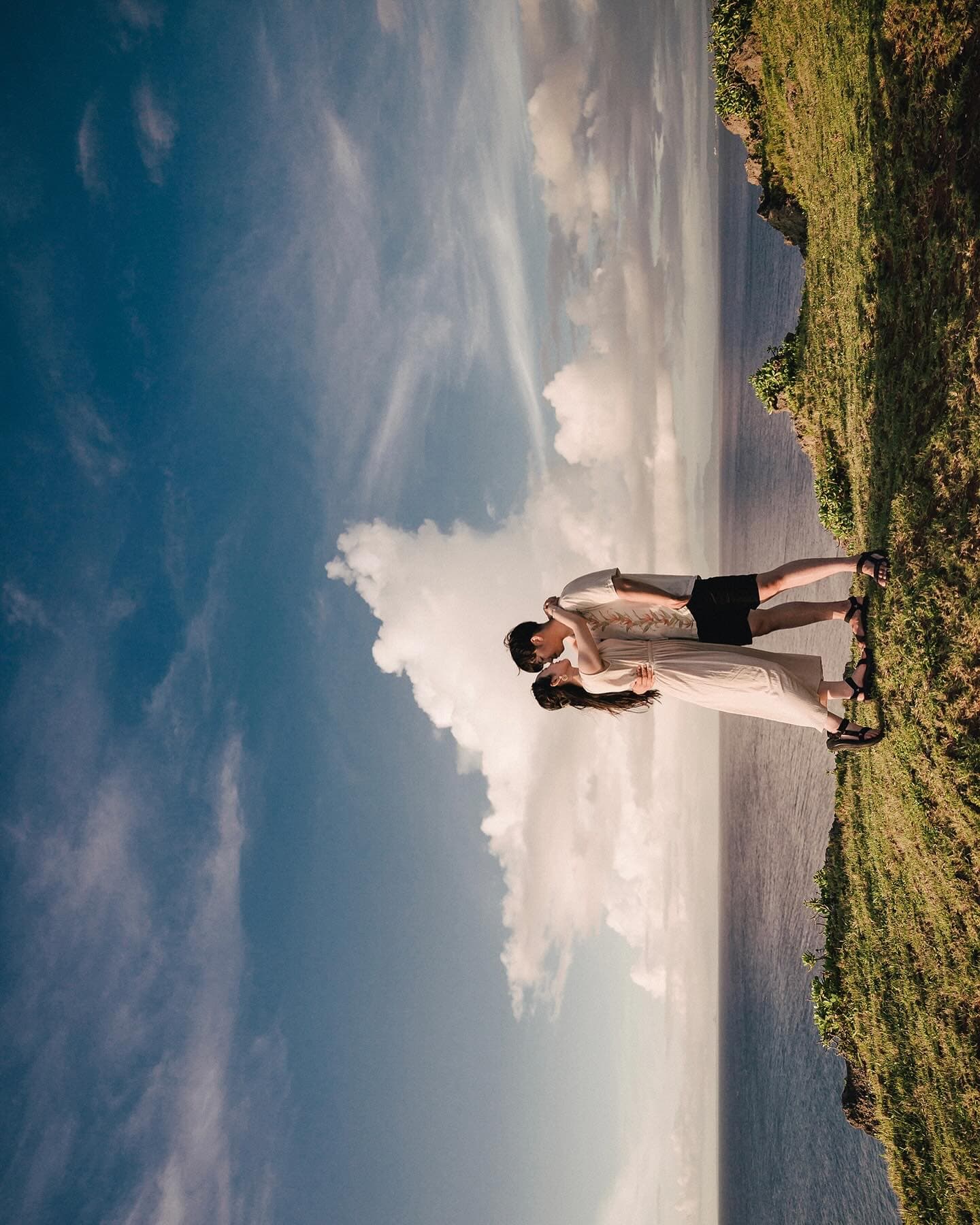 Couple close together on a coastal path under towering clouds in Okinawa