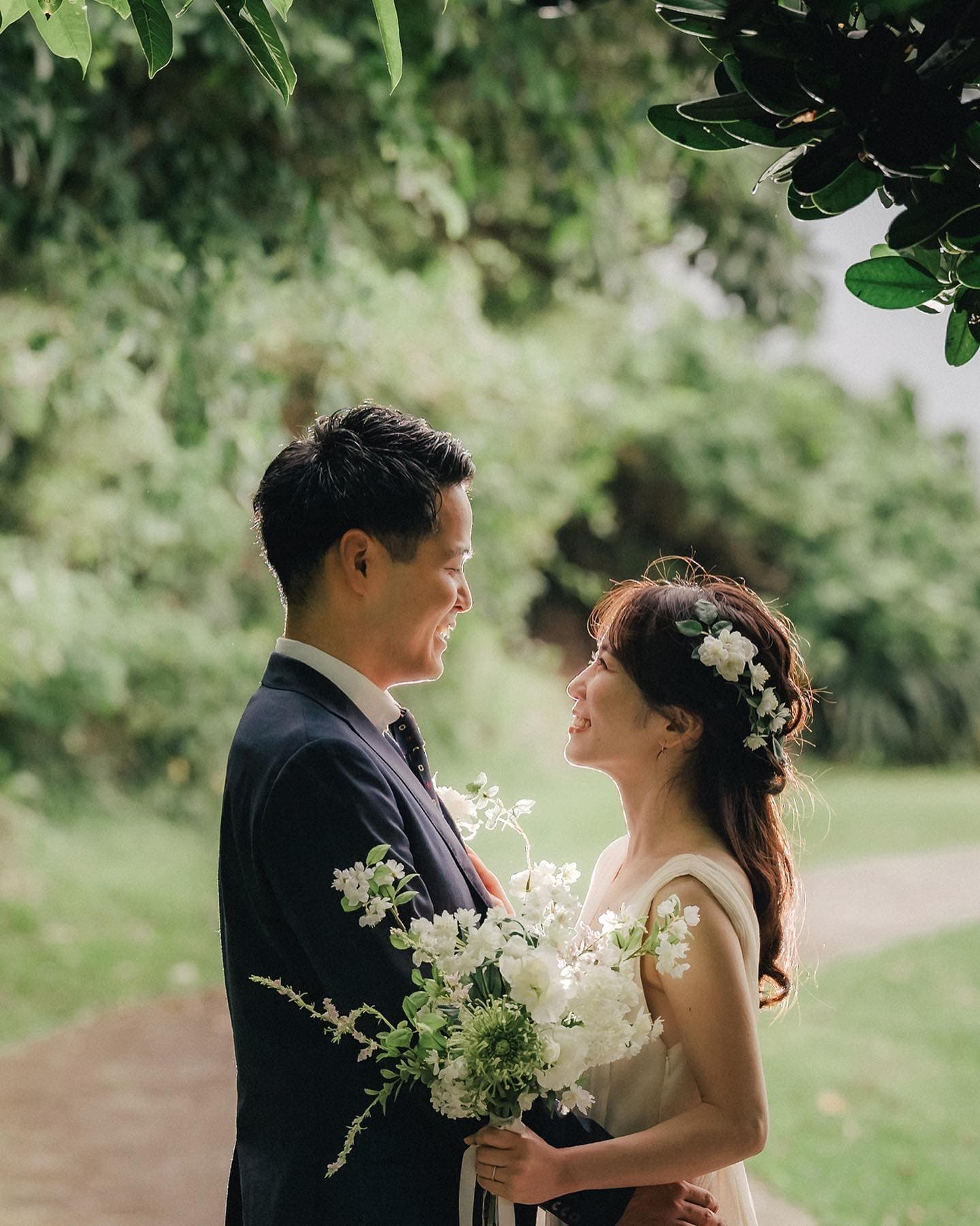Bride with a flower crown smiling at the groom under green trees in Okinawa