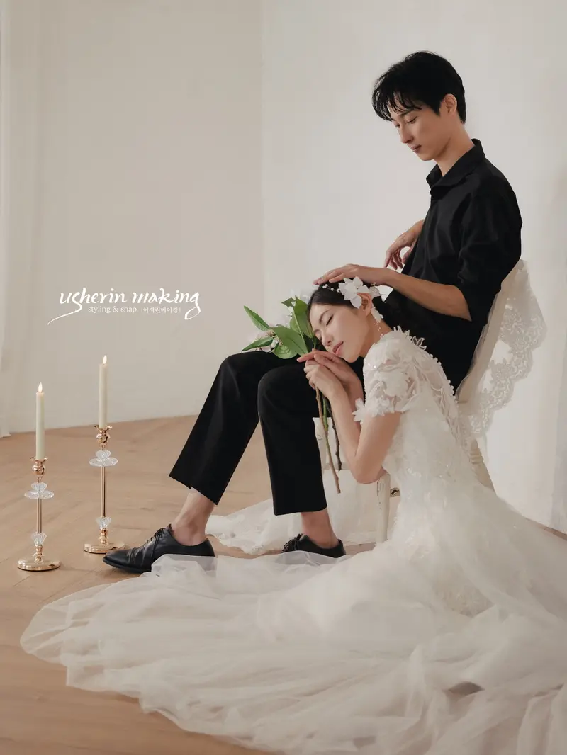 Bride resting against the seated groom's knee holding white tulips, candles lit in the studio