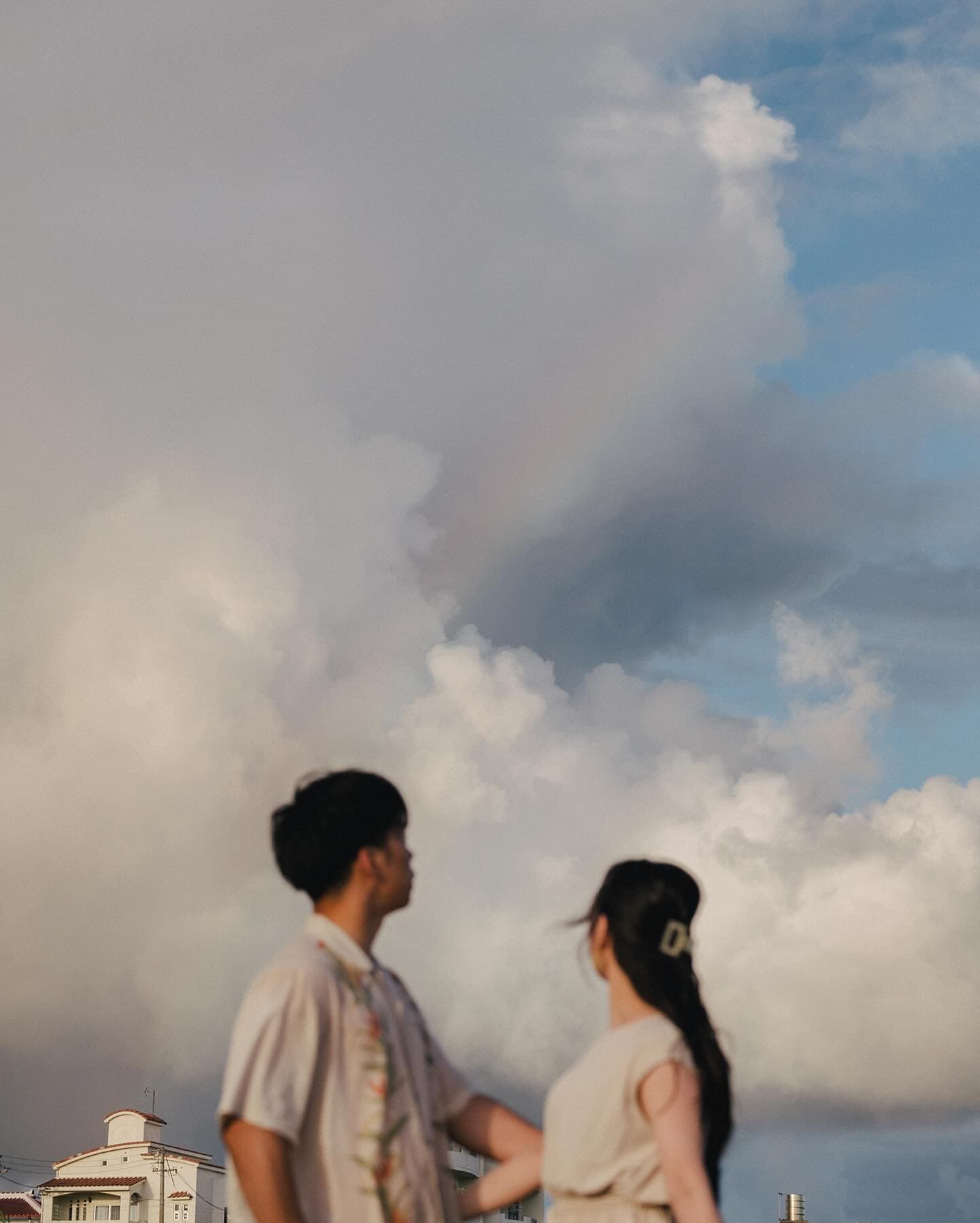 Couple gazing up at a rainbow among billowing clouds over an Okinawa town