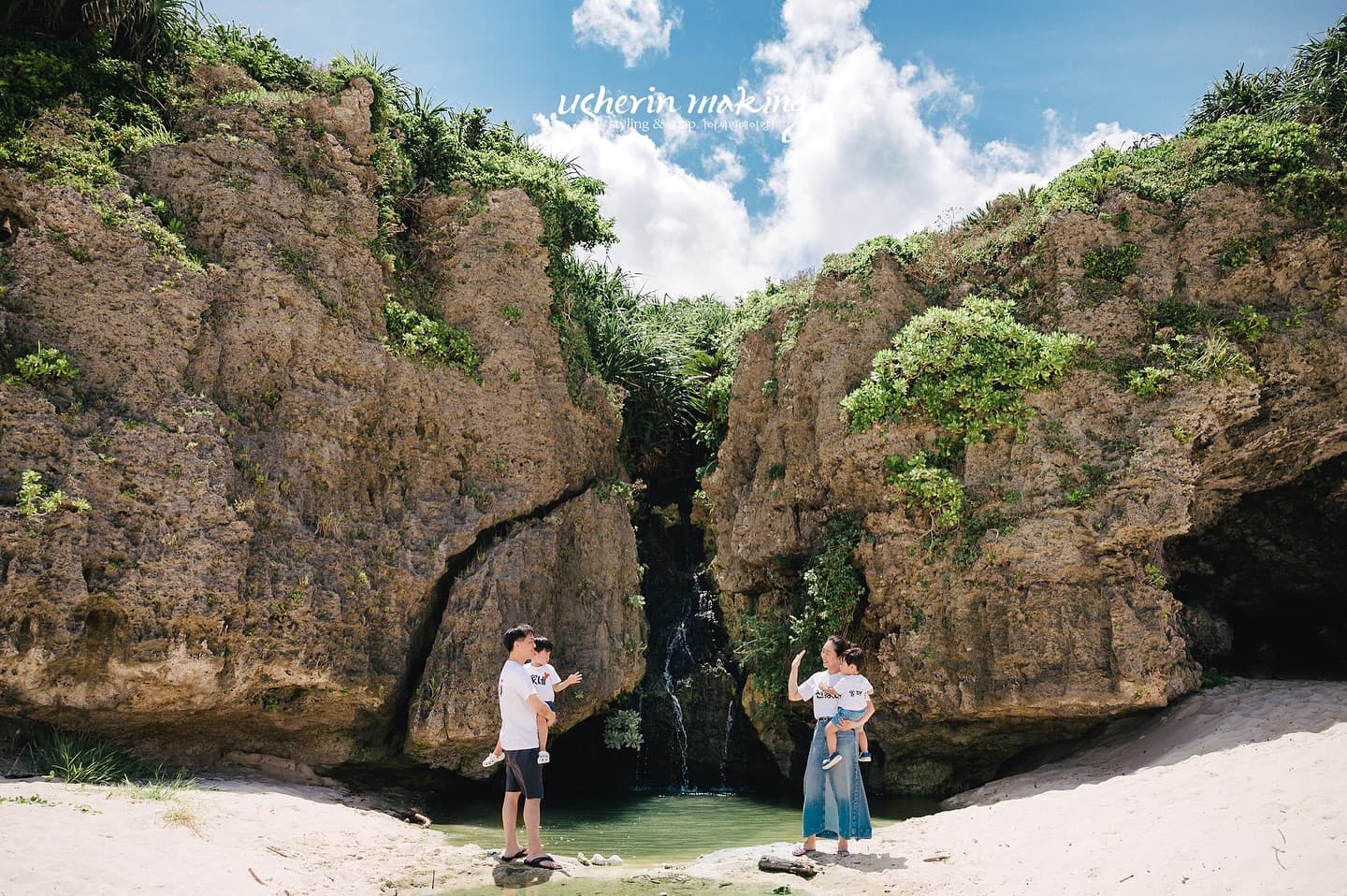 Parents hold their children before cliffs and a small waterfall in Okinawa