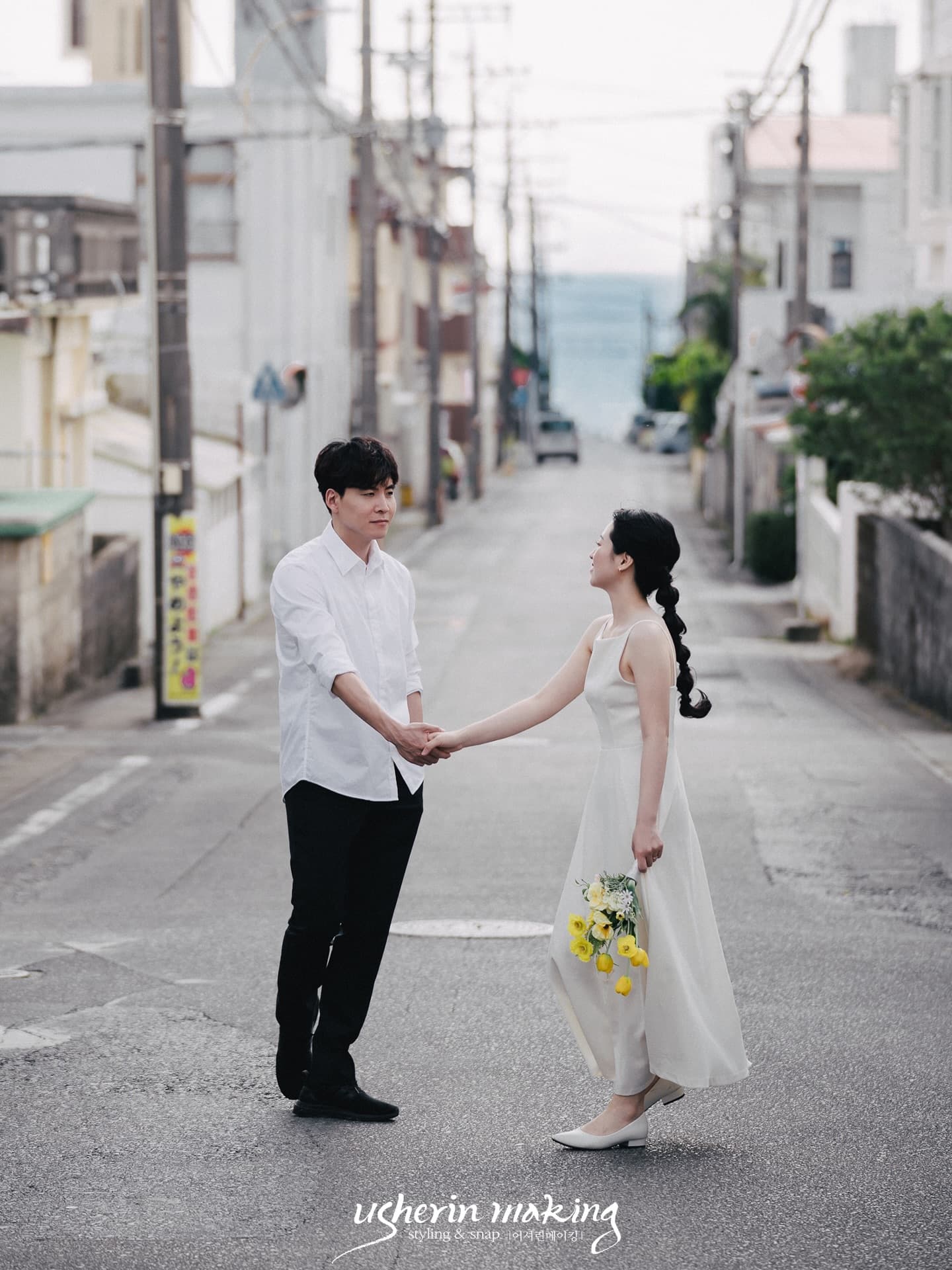 Couple holding hands on a quiet Okinawa town street that slopes down to the sea