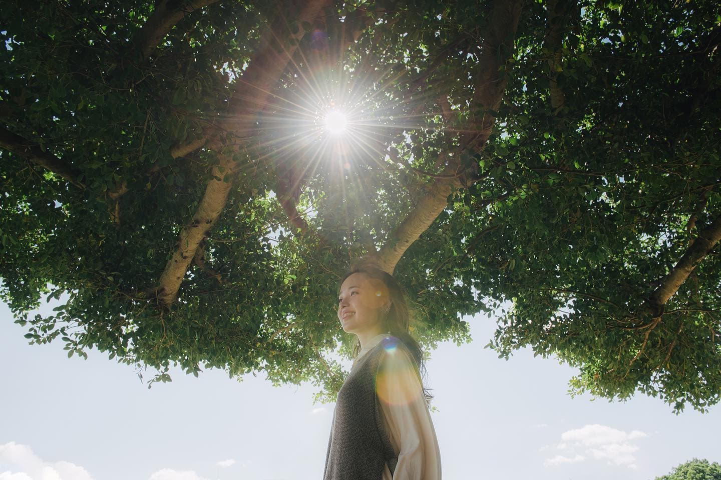 Woman beneath a large tree in Okinawa, sunlight bursting through the leaves