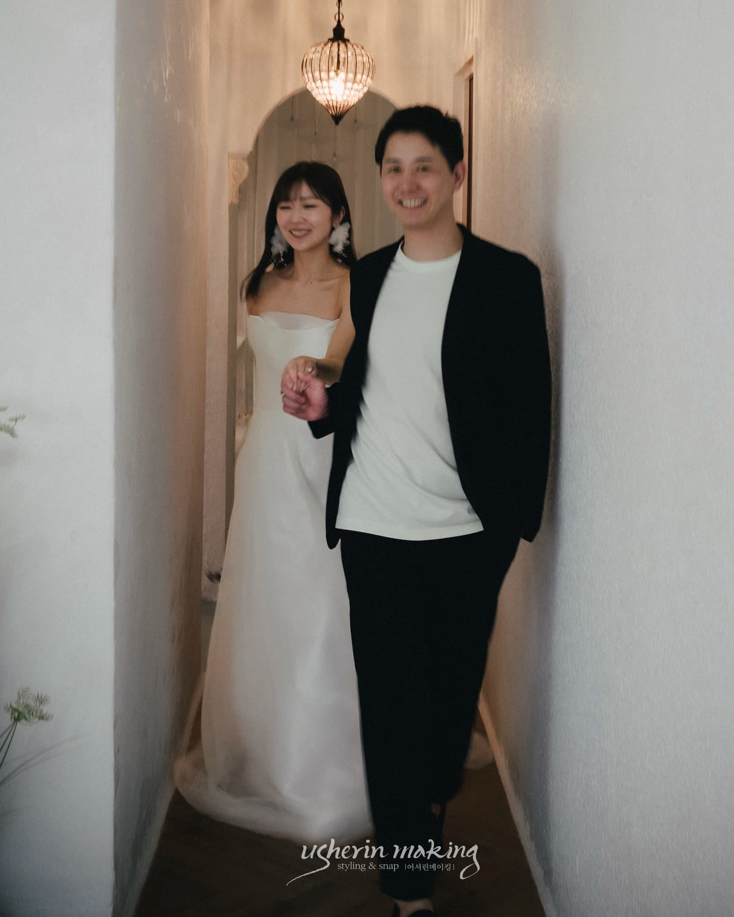 Bride and groom walking hand in hand down a white arched studio hallway