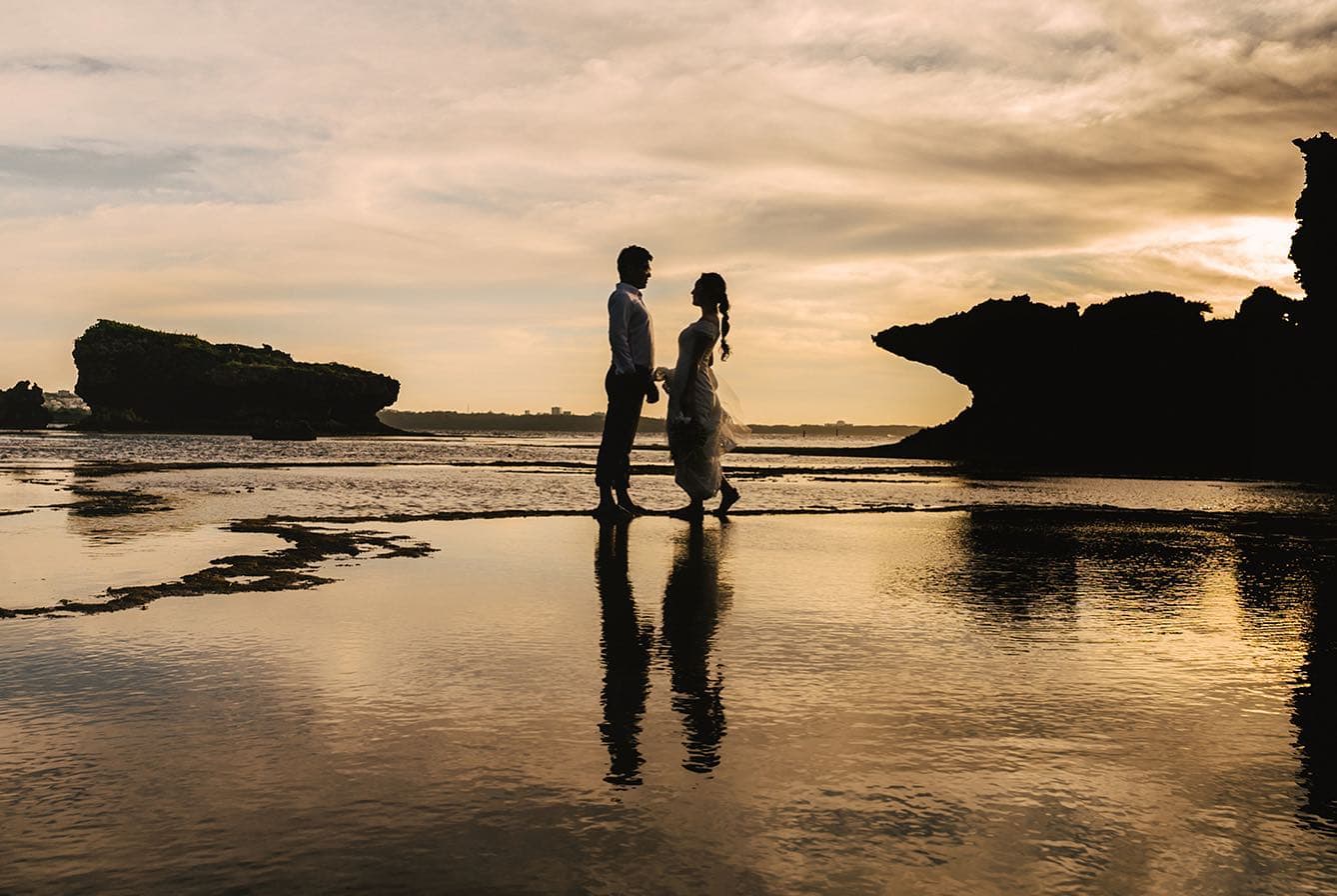 Silhouetted bride and groom walking across a tidal flat at sunset in Okinawa