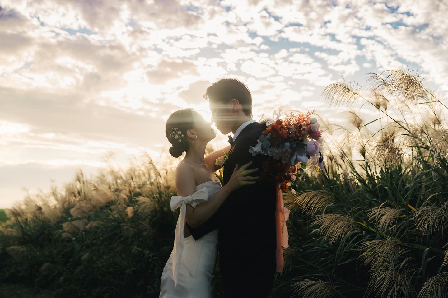 Couple embracing in a sunlit pampas grass field at sunset in Okinawa