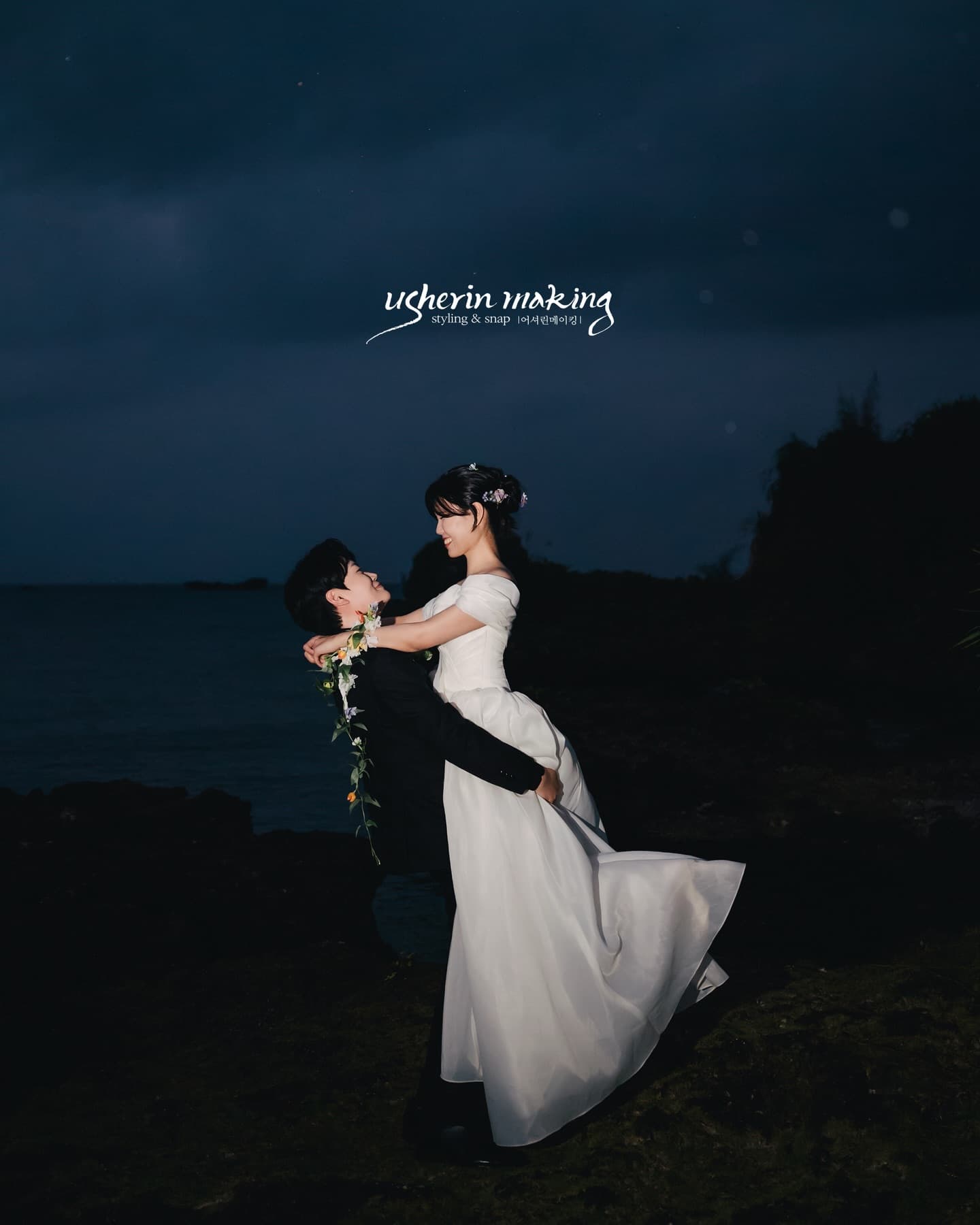 Groom dipping his bride on dark seaside rocks at night, Okinawa