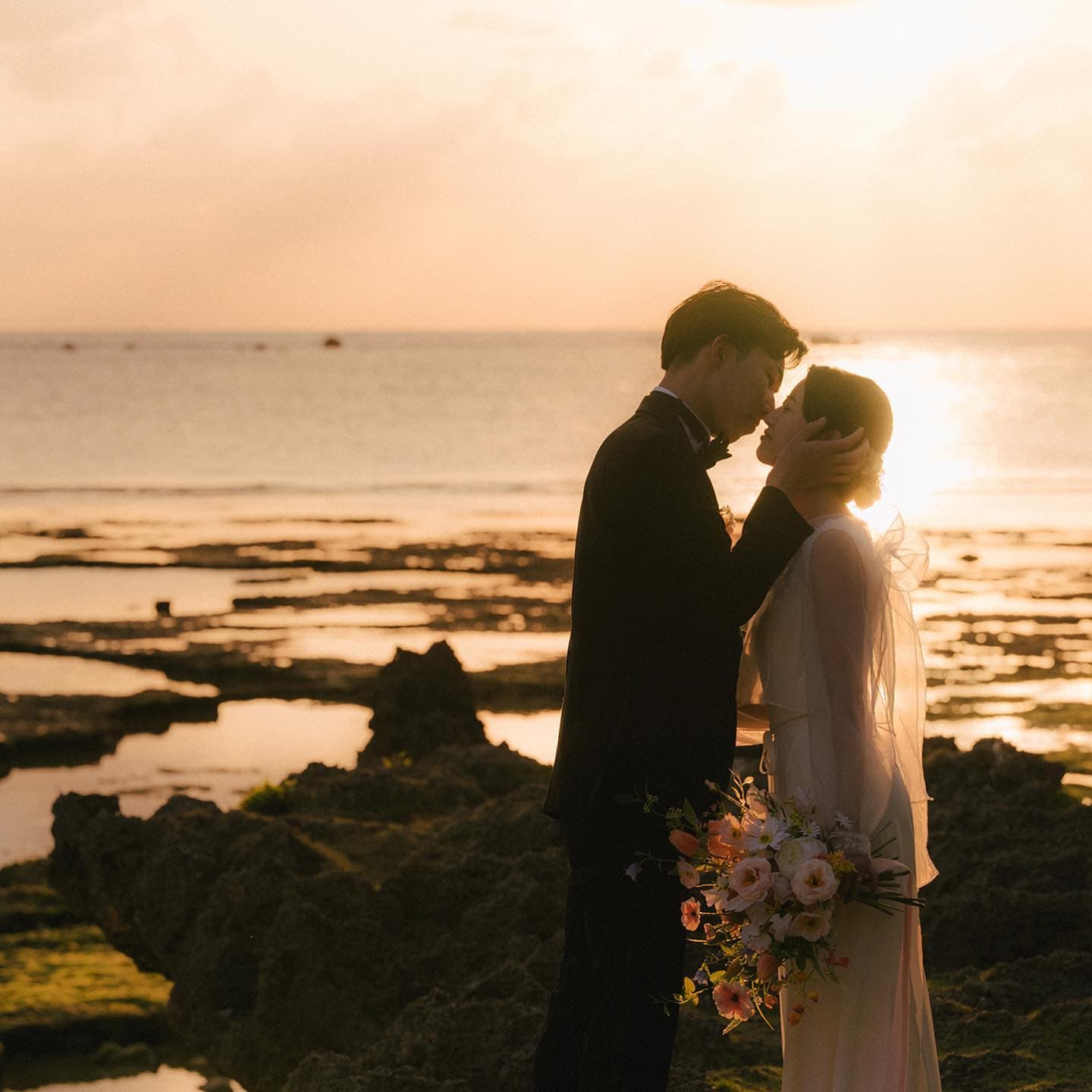 Bride and groom sharing a kiss above tide pools at sunset in Okinawa