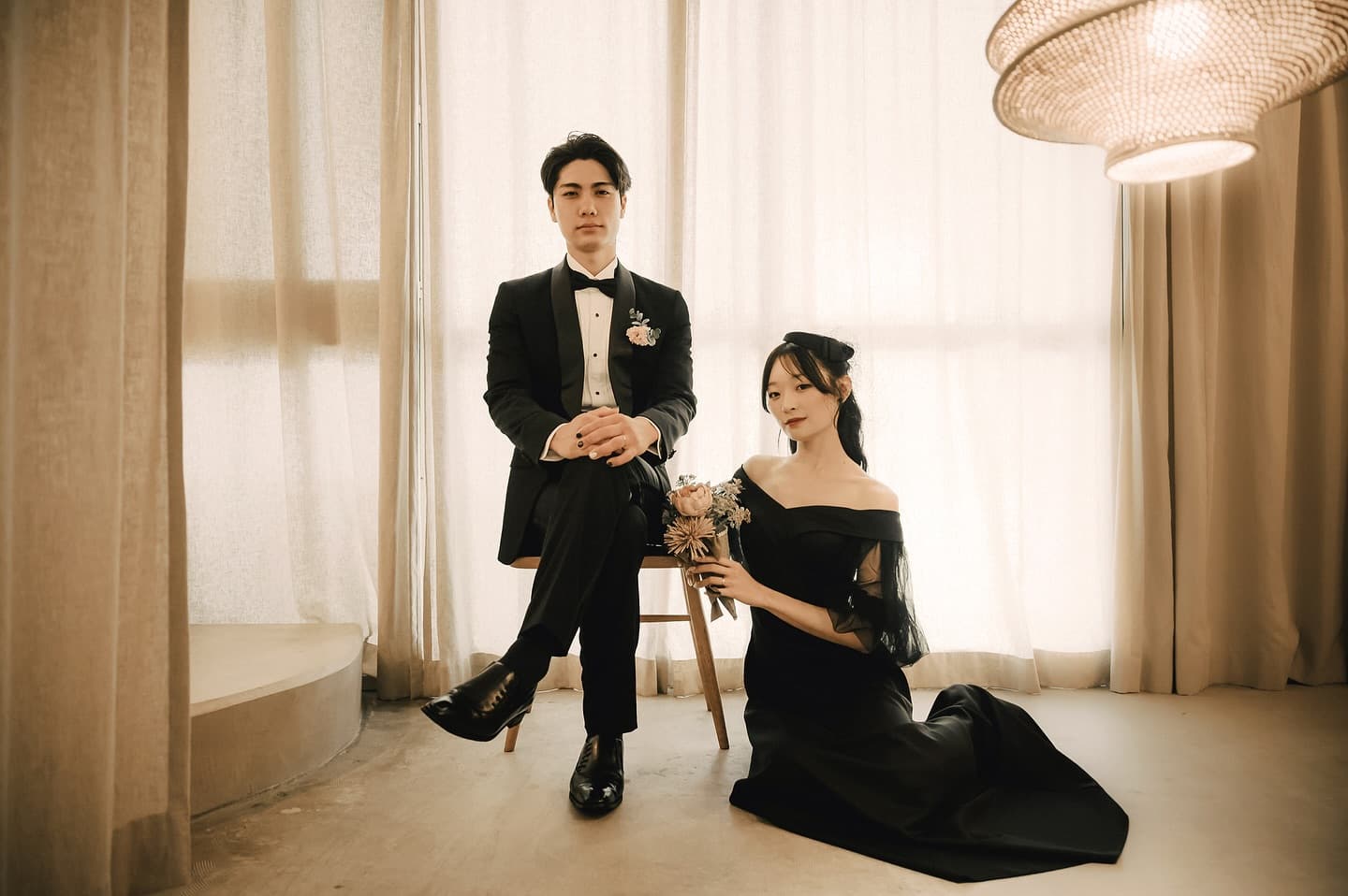Couple in a black tuxedo and dress posing in a softly lit studio set