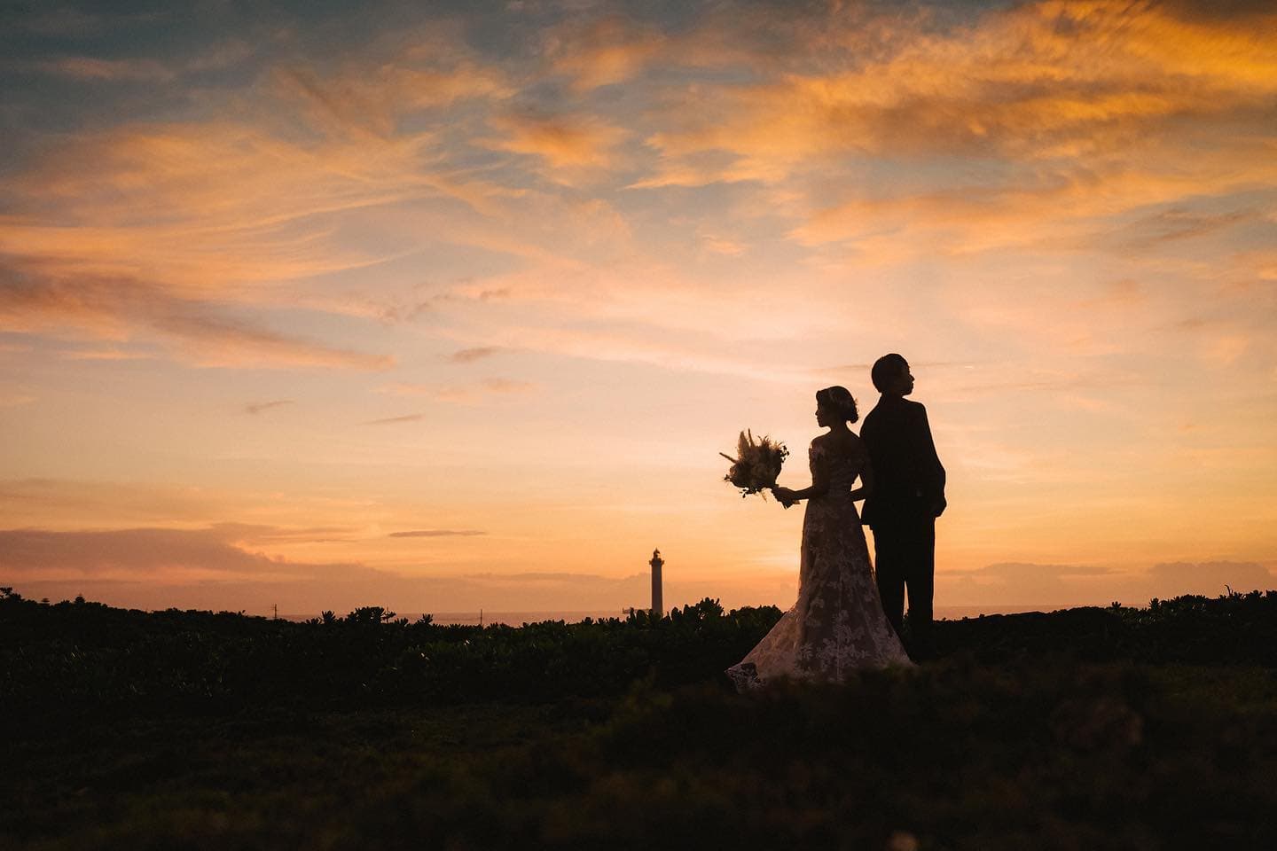 Silhouetted couple stand against a fiery sunset sky near an Okinawa lighthouse