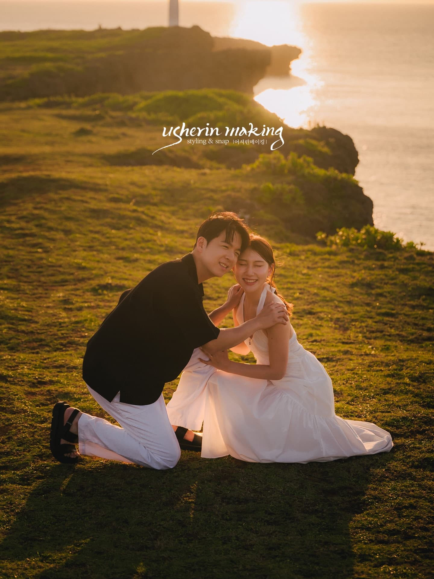 Couple nestling together on a grassy cape with a lighthouse and golden sea, Okinawa