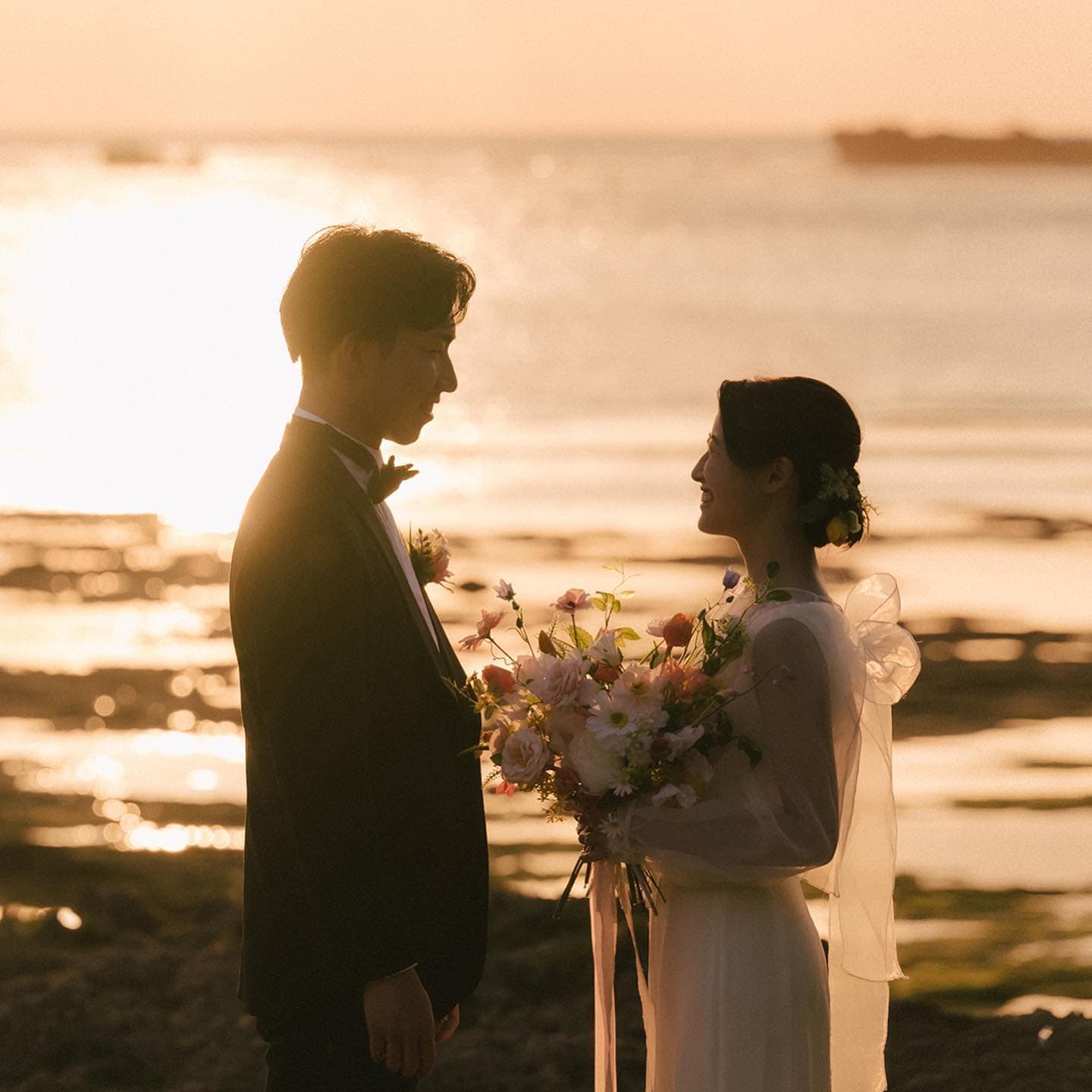 Couple facing each other with a bouquet on an Okinawa beach glowing at sunset