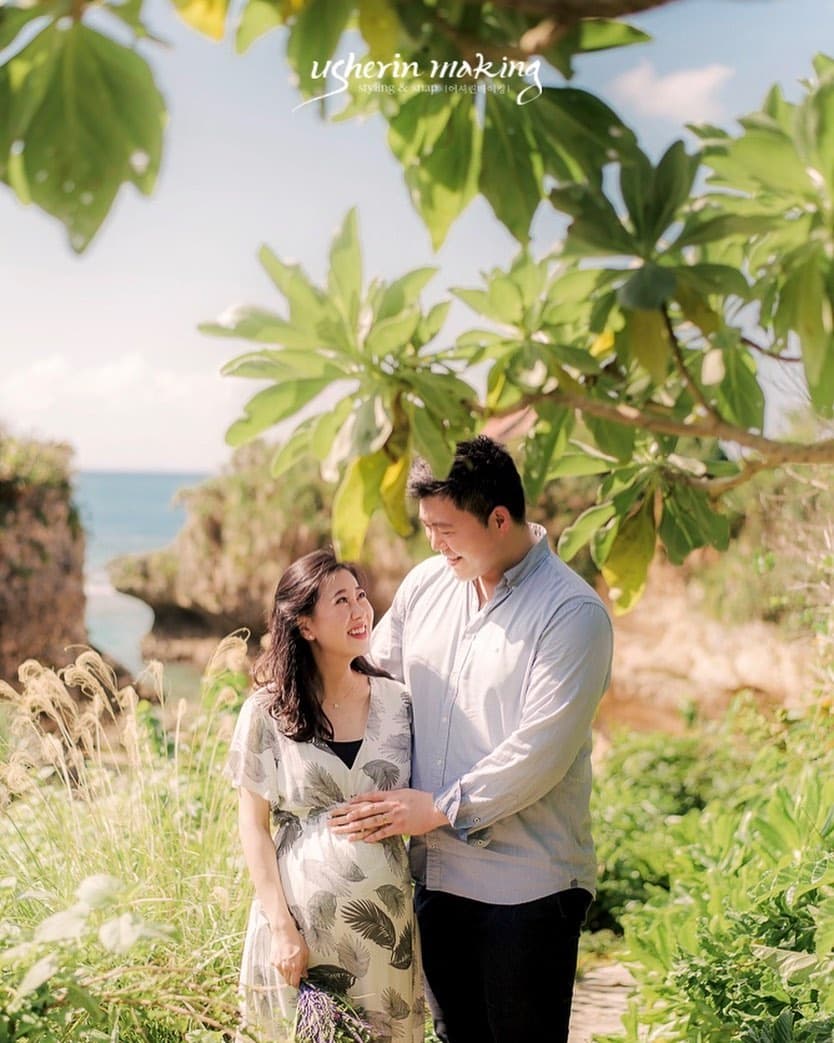 Expecting couple smiling at each other among lush greenery by the sea in Okinawa