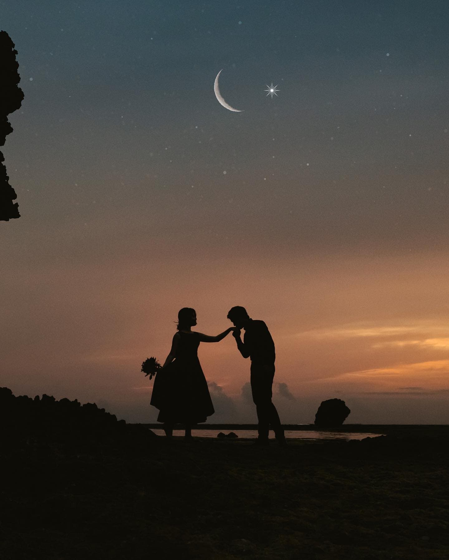 三日月が浮かぶ夕暮れの沖縄の浜辺で、花嫁の手にキスをする新郎のシルエット
