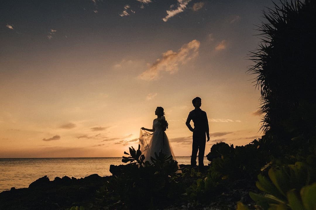 オレンジ色の夕焼け空を背にした沖縄の海辺の新郎新婦のシルエット