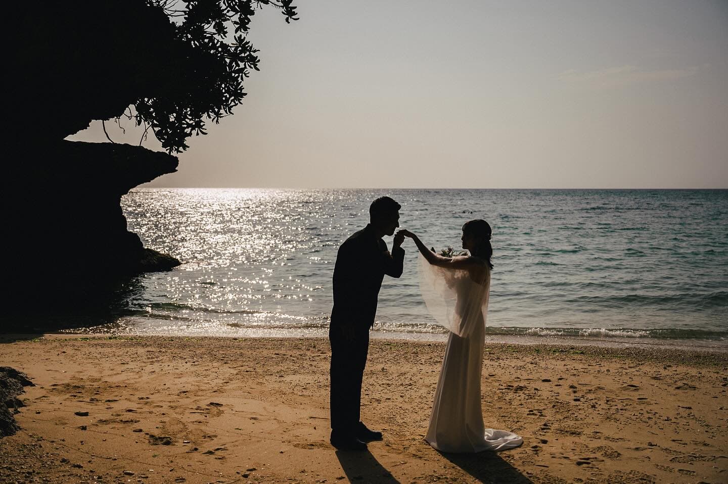 Groom kissing the bride's hand in silhouette by the Okinawa sea