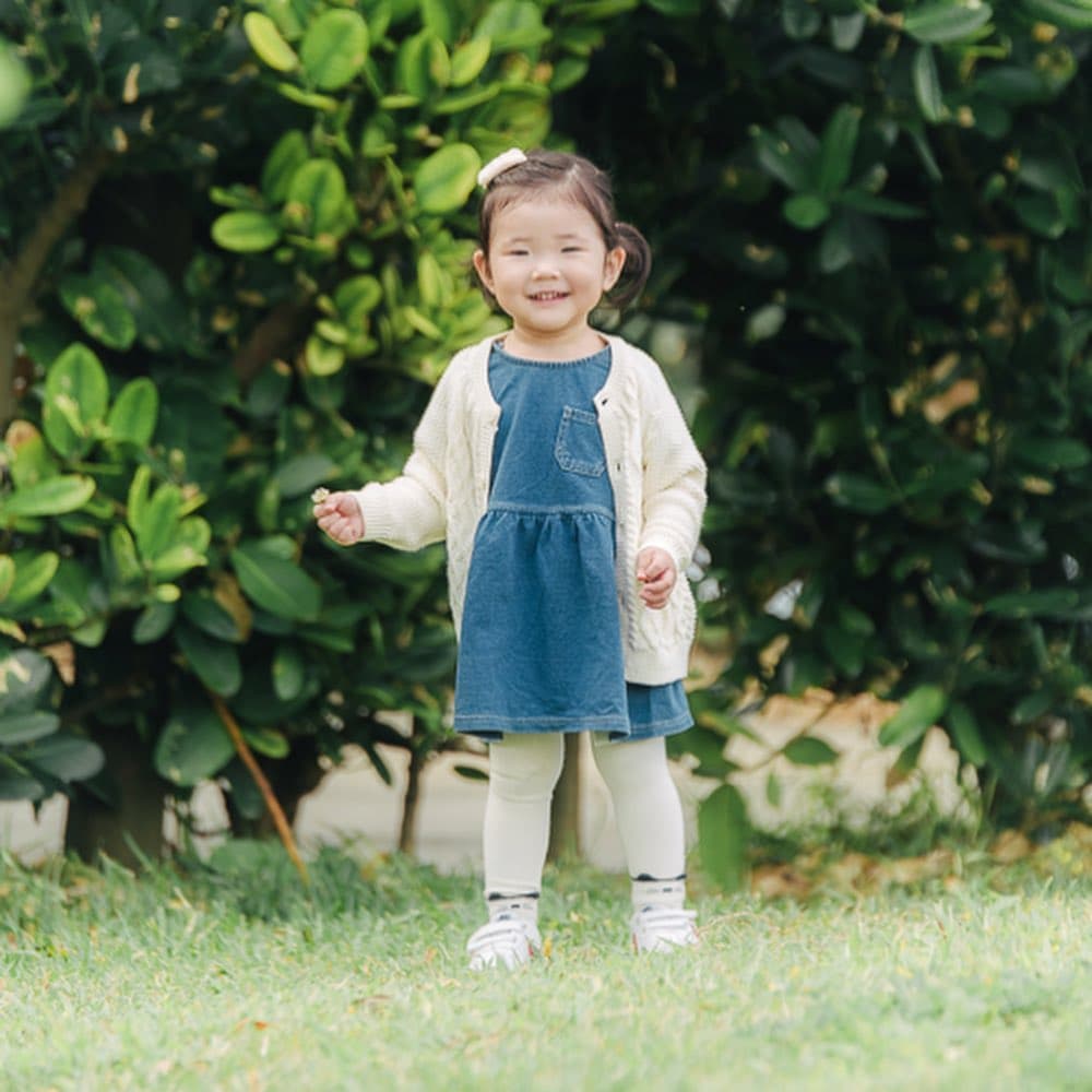 A smiling toddler girl holds a tiny flower on a green lawn in Okinawa