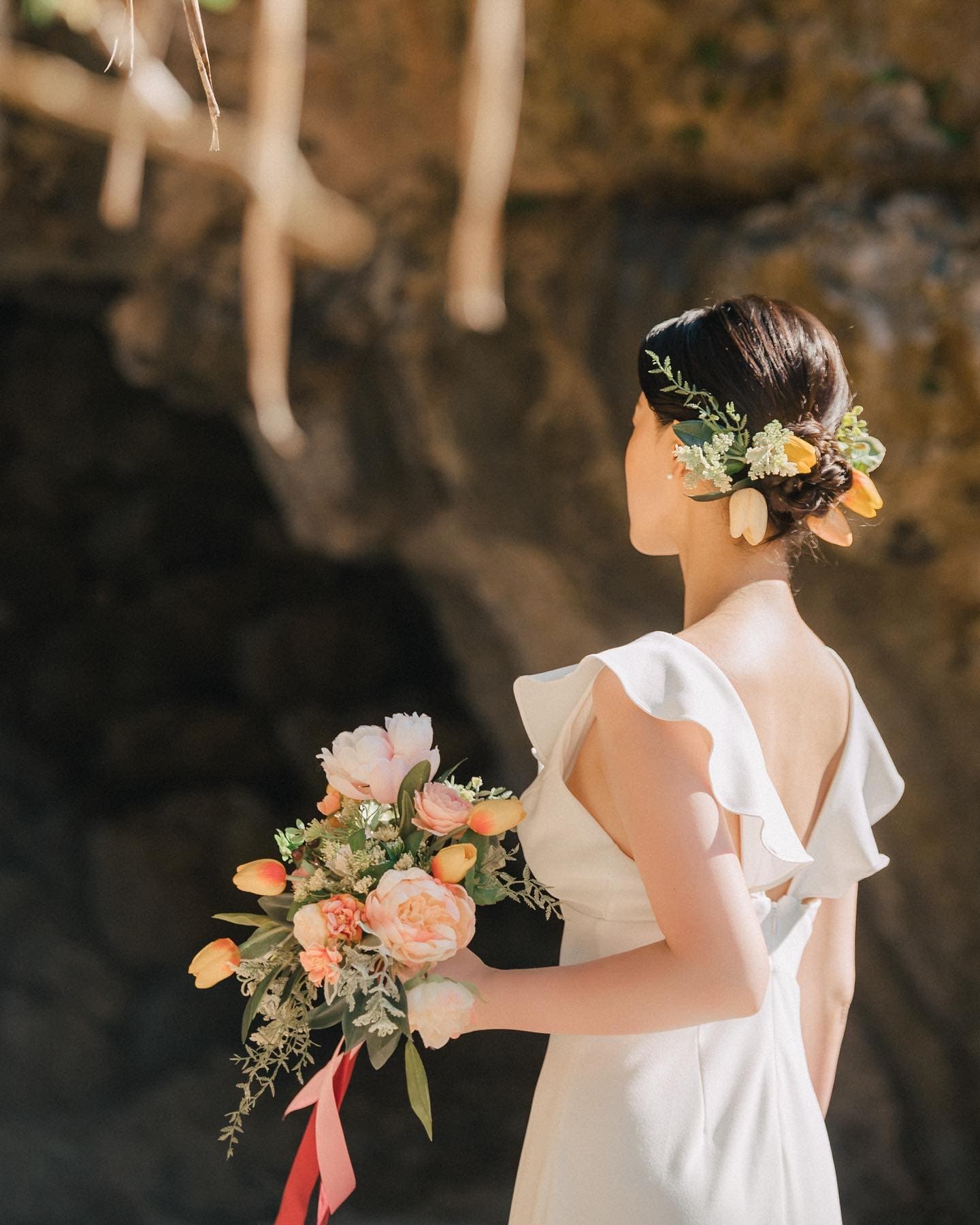 チューリップのブーケと髪飾りをつけた花嫁の後ろ姿。沖縄の岩場にて。