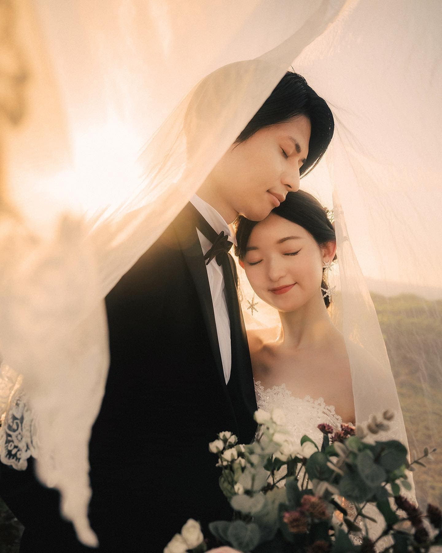ベールに包まれ夕焼けの光の中で寄り添う新郎新婦