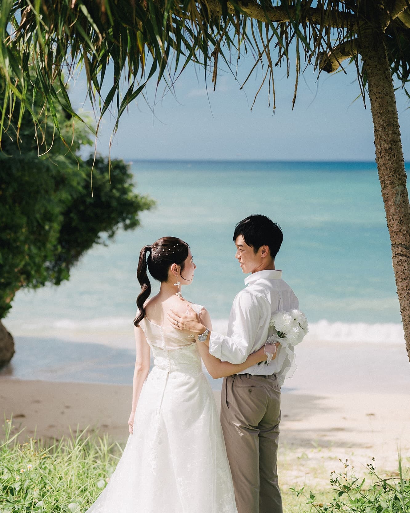 Couple gazing at each other under a palm tree by the Okinawa sea