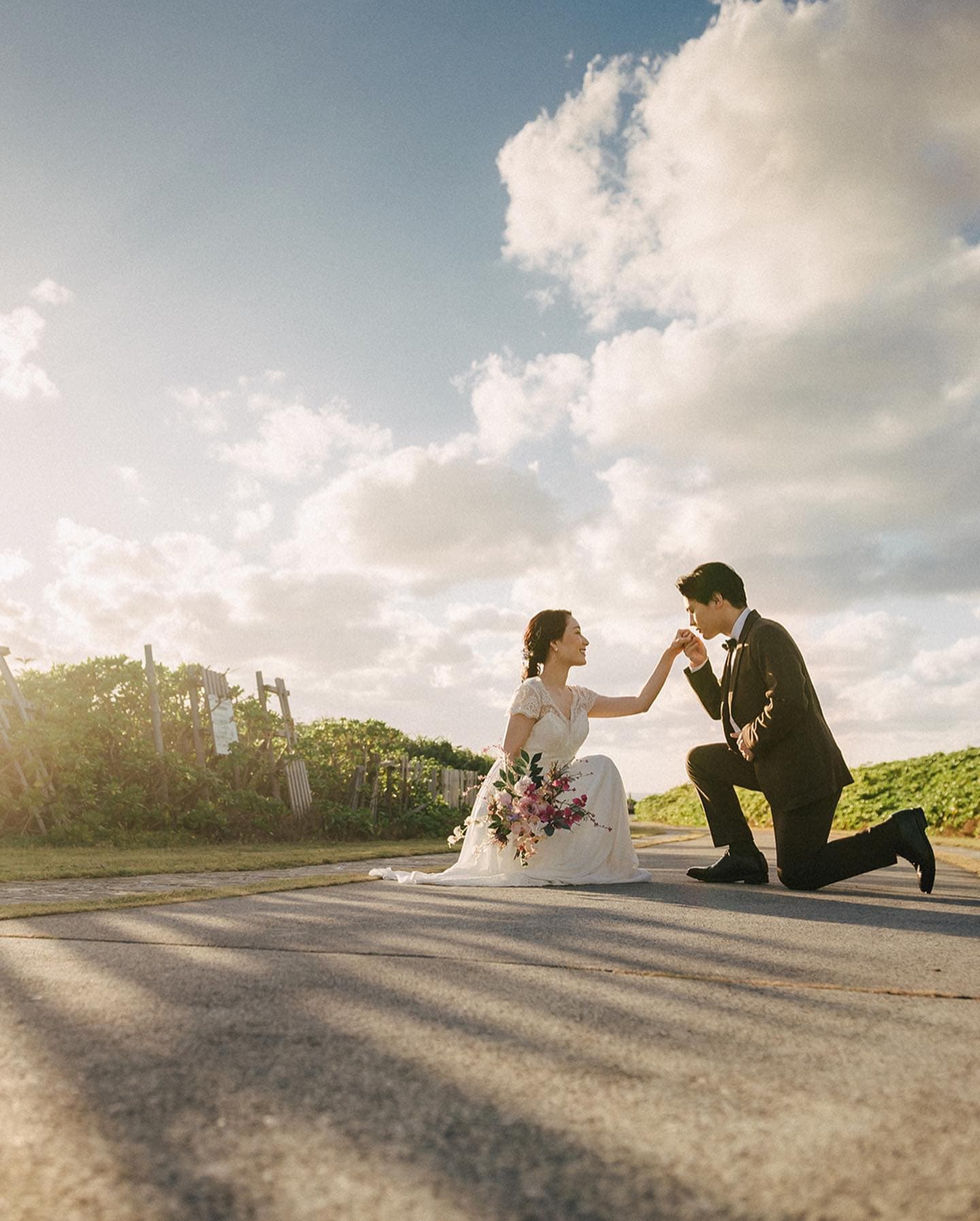 Groom kneeling to kiss his bride's hand on an open Okinawa road at golden hour