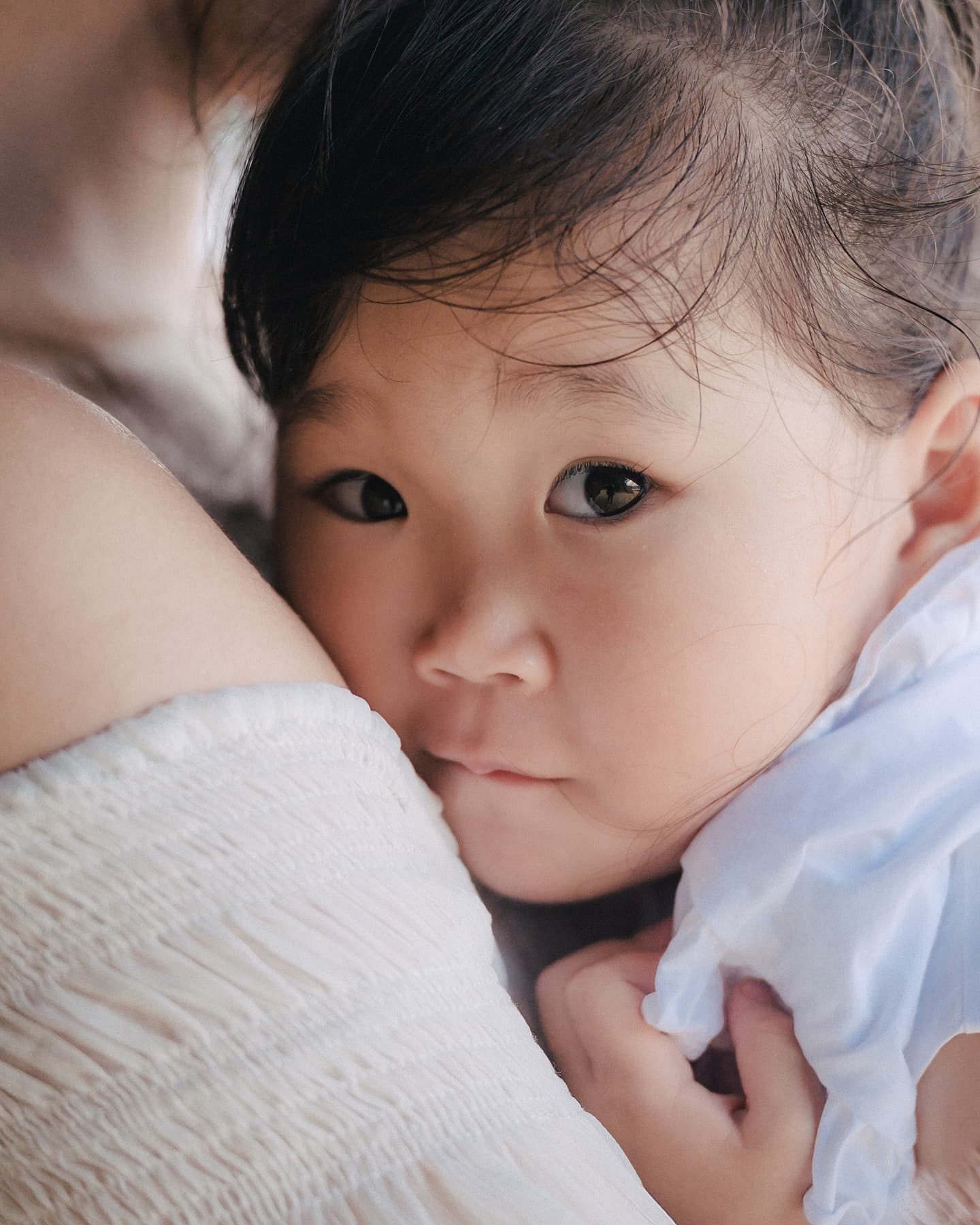 Toddler girl gazing at the camera from her mother's arms in Okinawa
