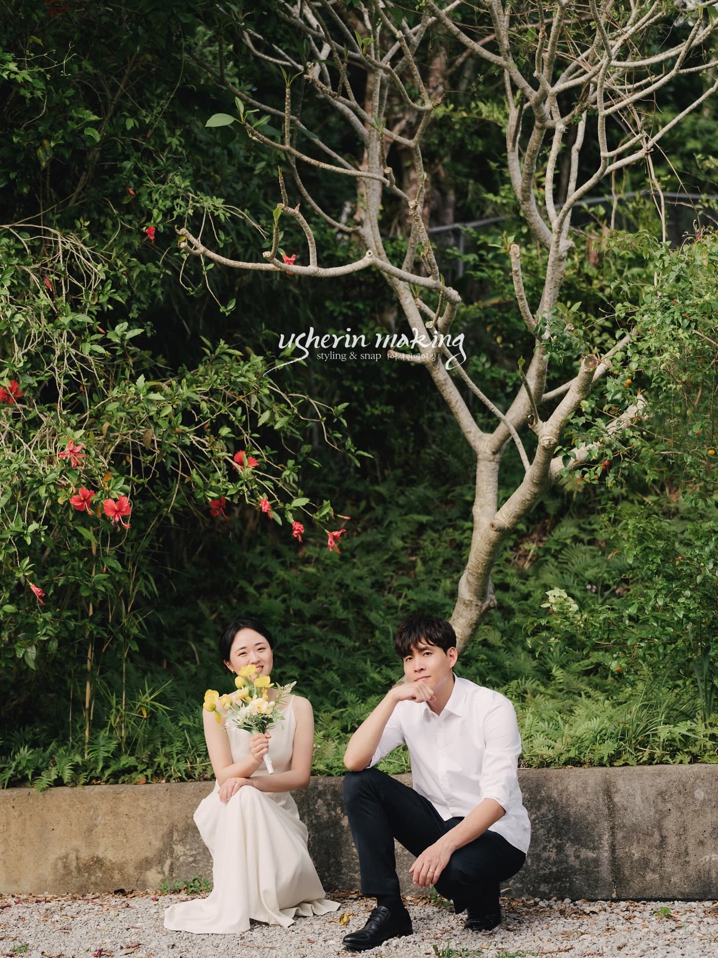 Bride and groom crouching to pose in a garden with red hibiscus in Okinawa