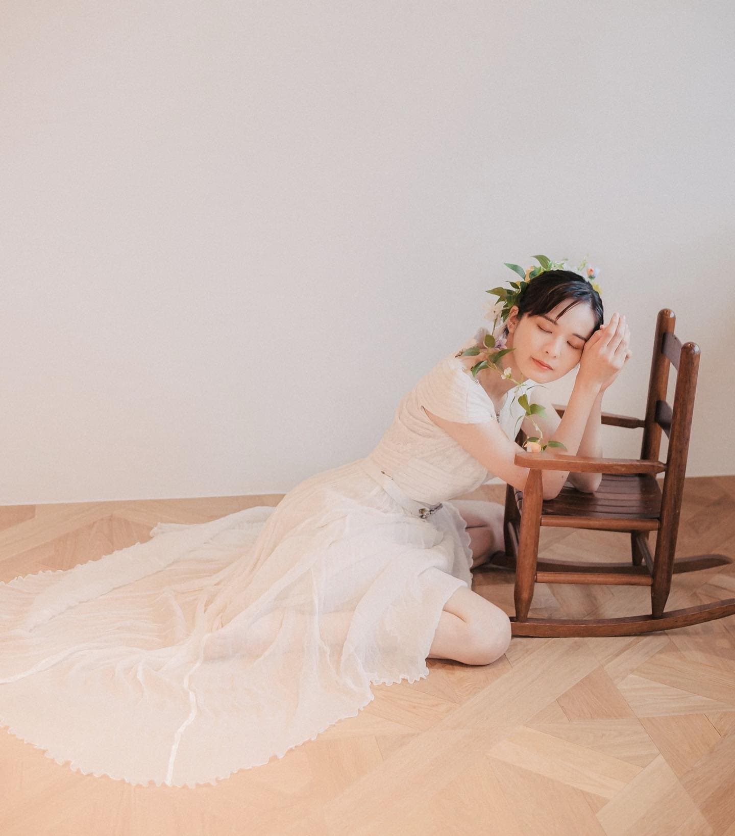 Bride in a white dress resting her eyes against a wooden rocking chair in the studio