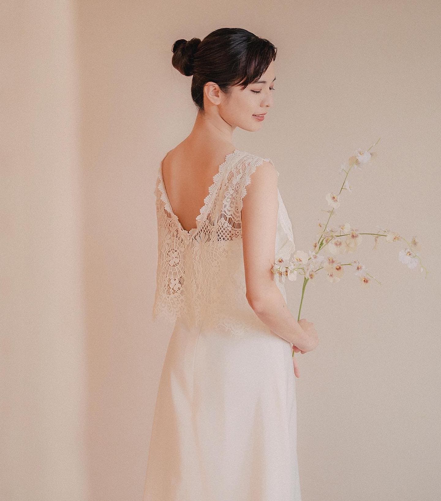 Back view of a bride in a lace-backed dress holding a stem of orchids