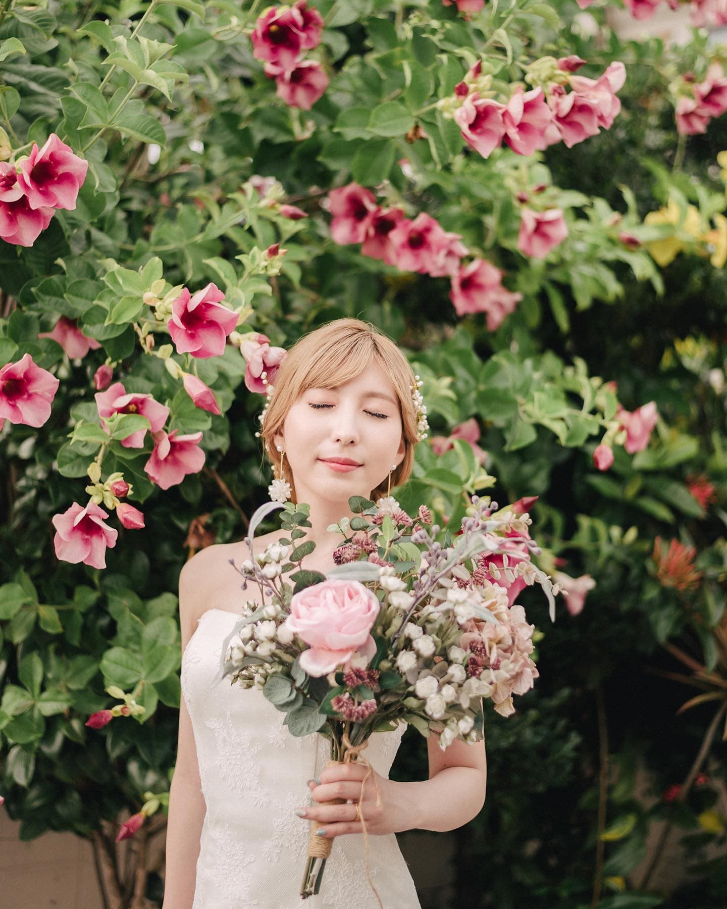 Bride with closed eyes holding a bouquet before a wall of pink blossoms in Okinawa