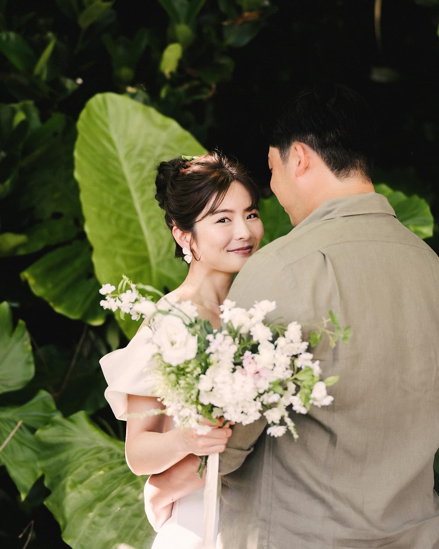Bride smiles over the groom's shoulder amid Okinawa greenery