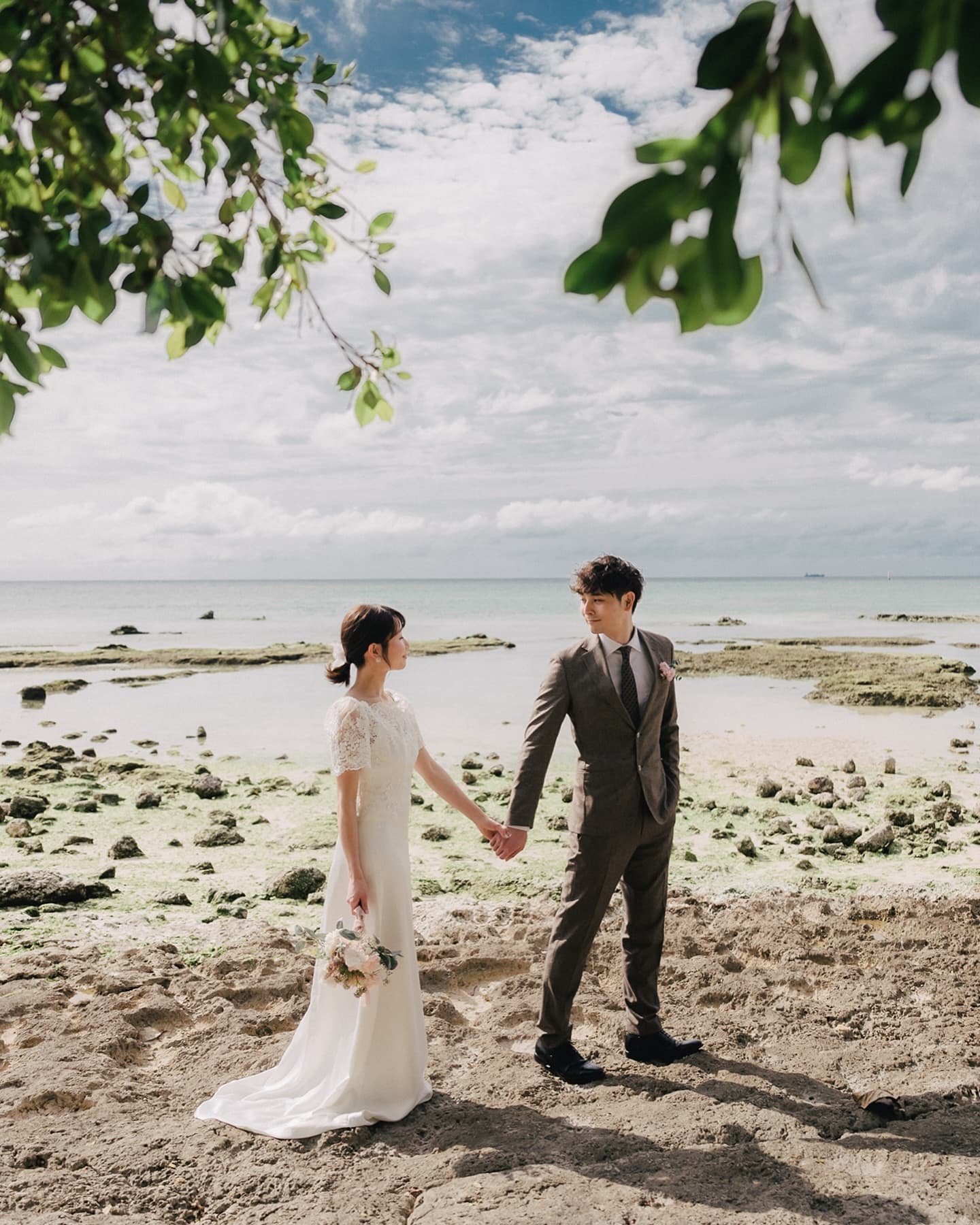Bride and groom holding hands by the emerald sea under a blue sky in Okinawa