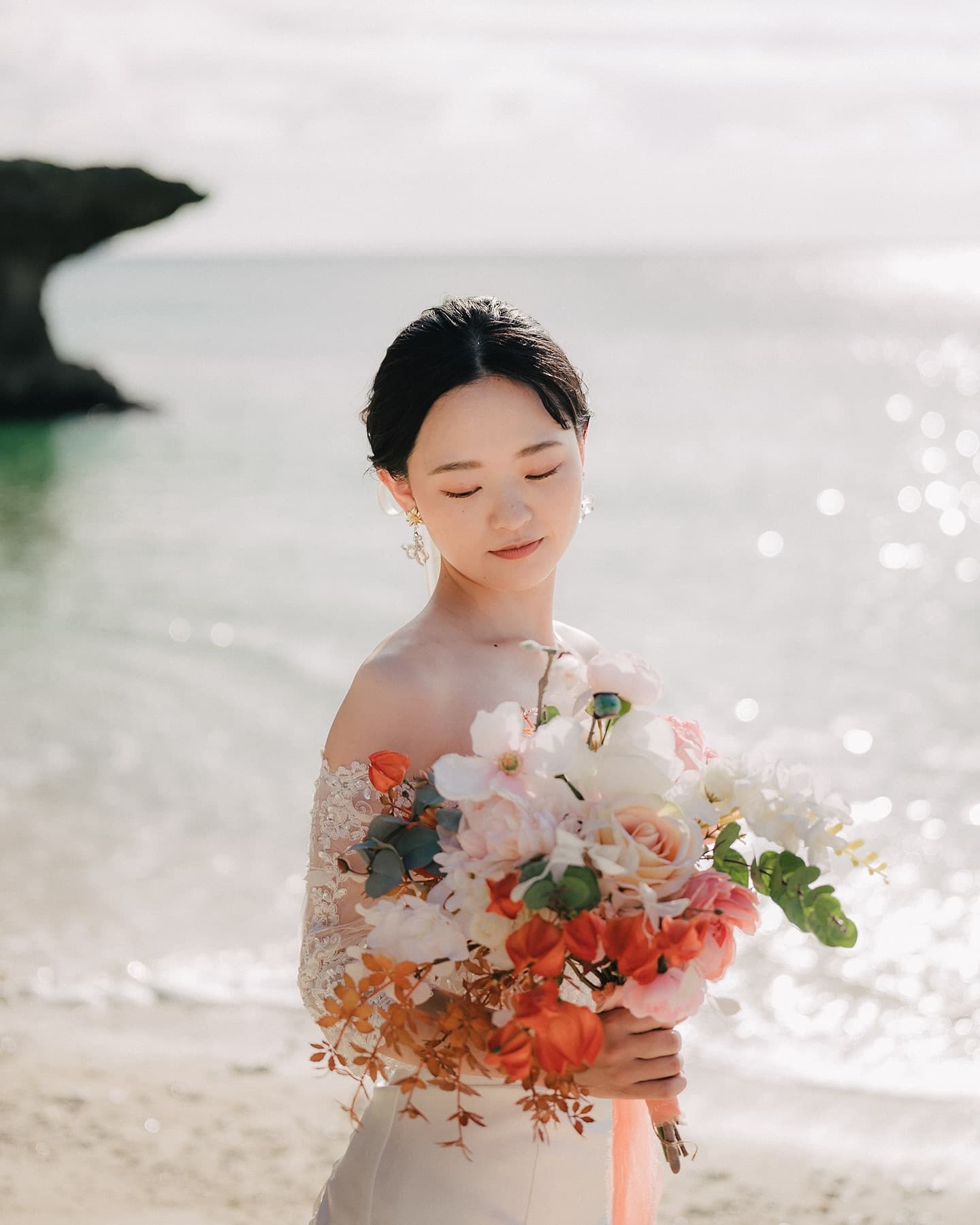 きらめく海を背に目を閉じてブーケを抱く花嫁のポートレート、沖縄