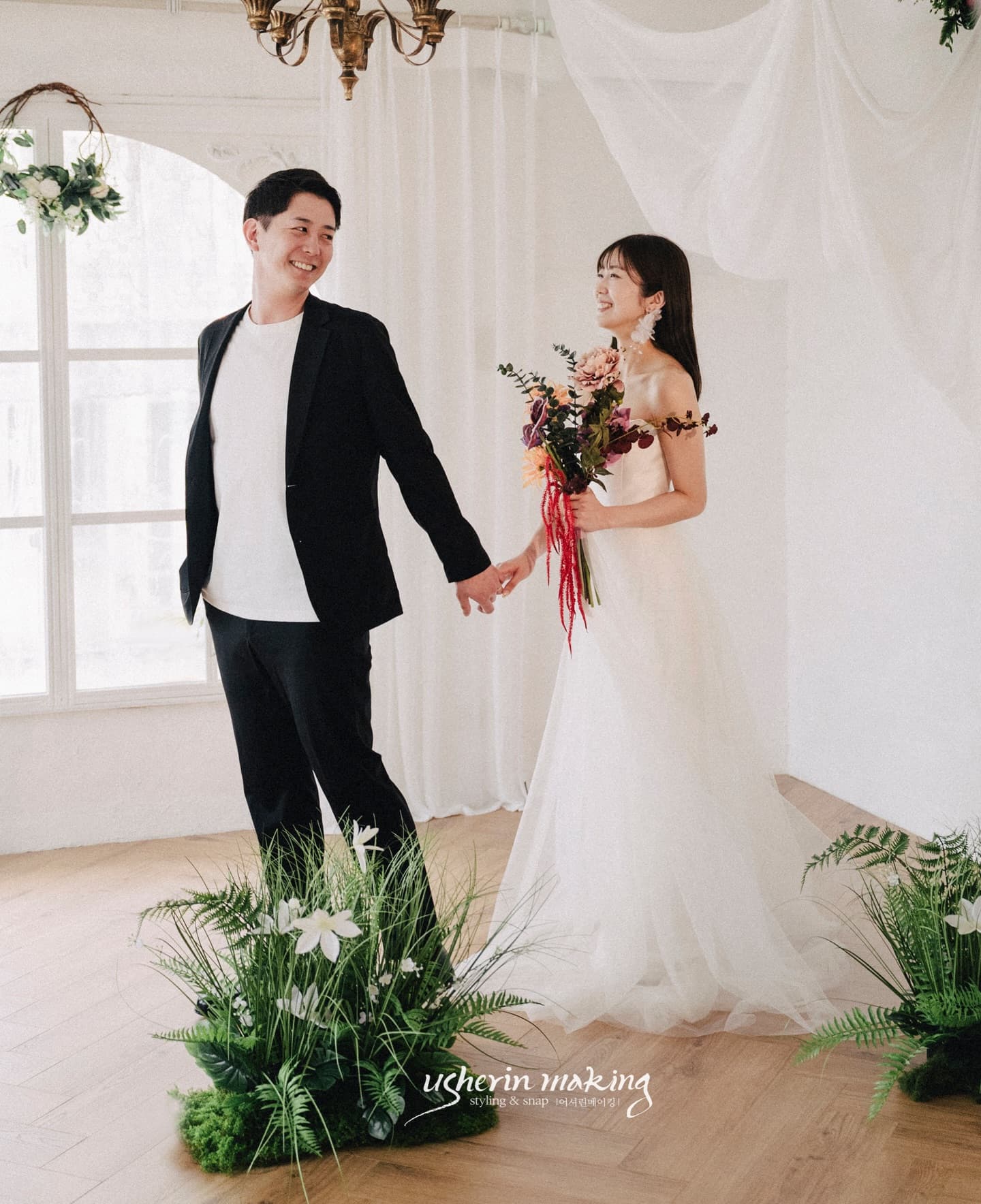 아치 창과 그린 장식의 화이트 스튜디오에서 손잡은 신랑신부