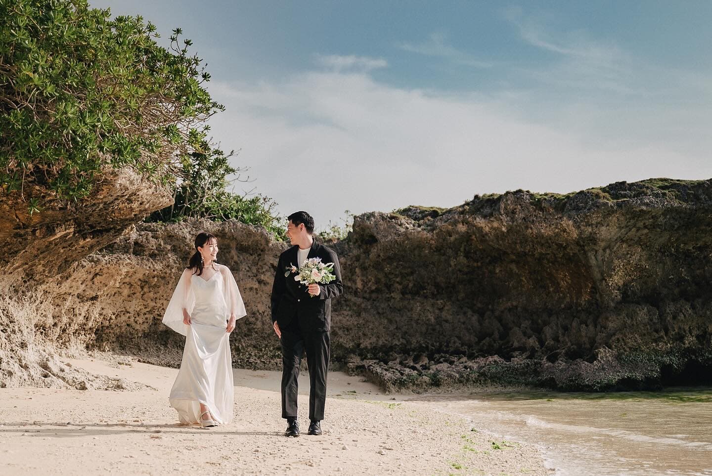 Wide shot of newlyweds walking together on a rocky Okinawa beach