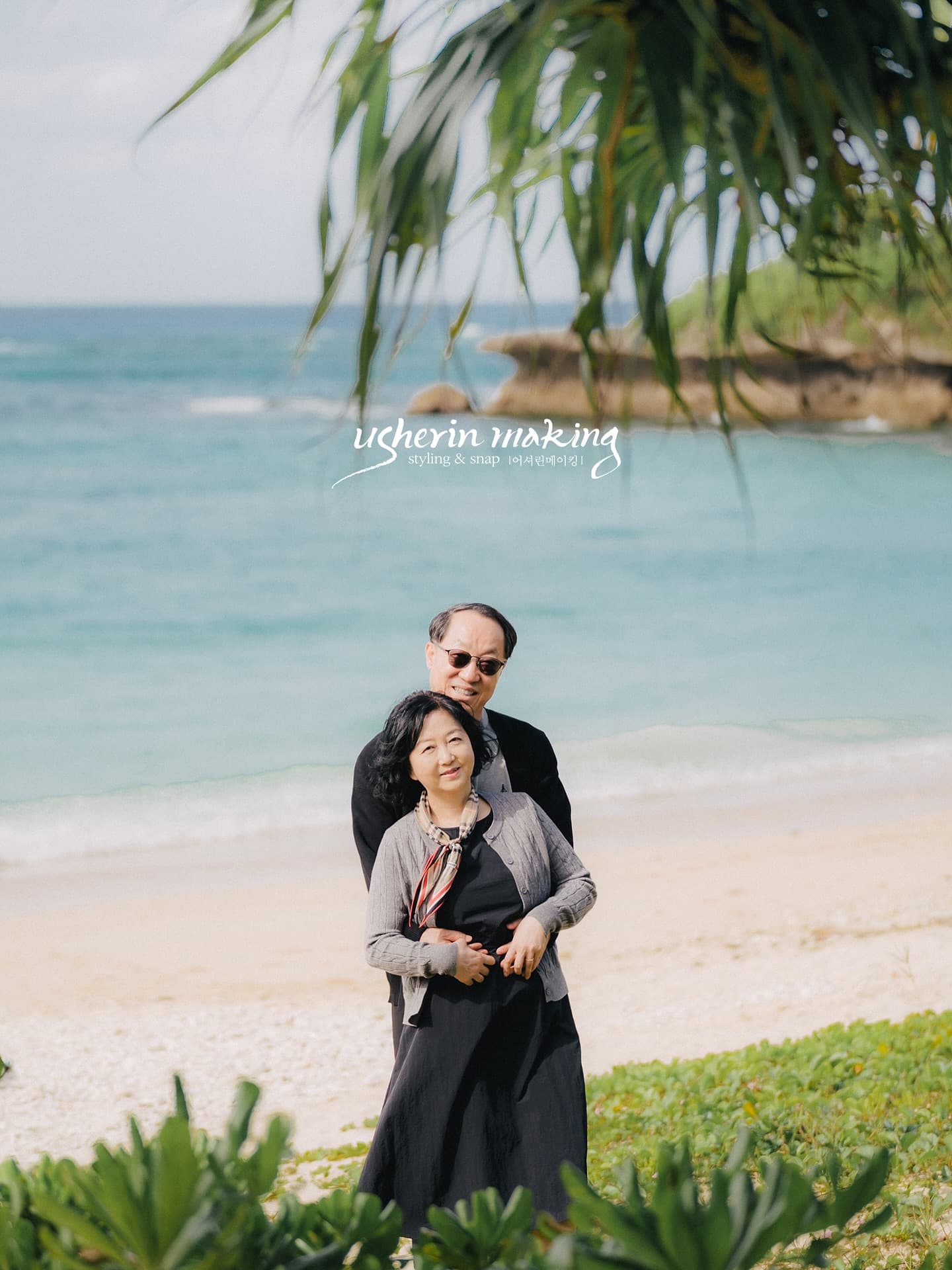 Older couple posing together by the emerald sea on a sunny Okinawa beach