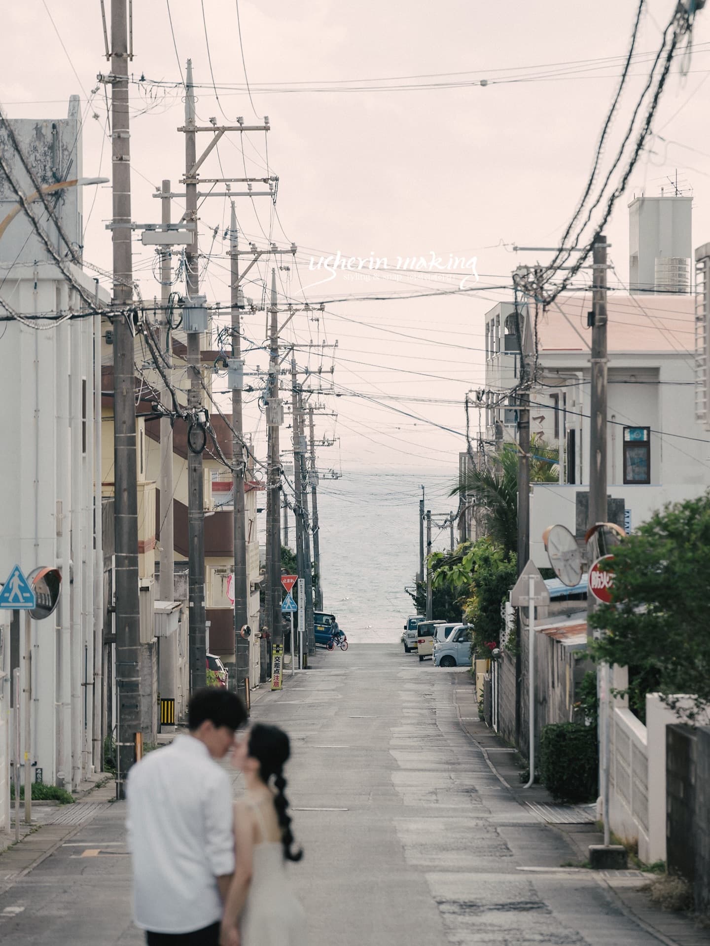 Couple close together on an Okinawa street lined with power poles, the sea at the road's end