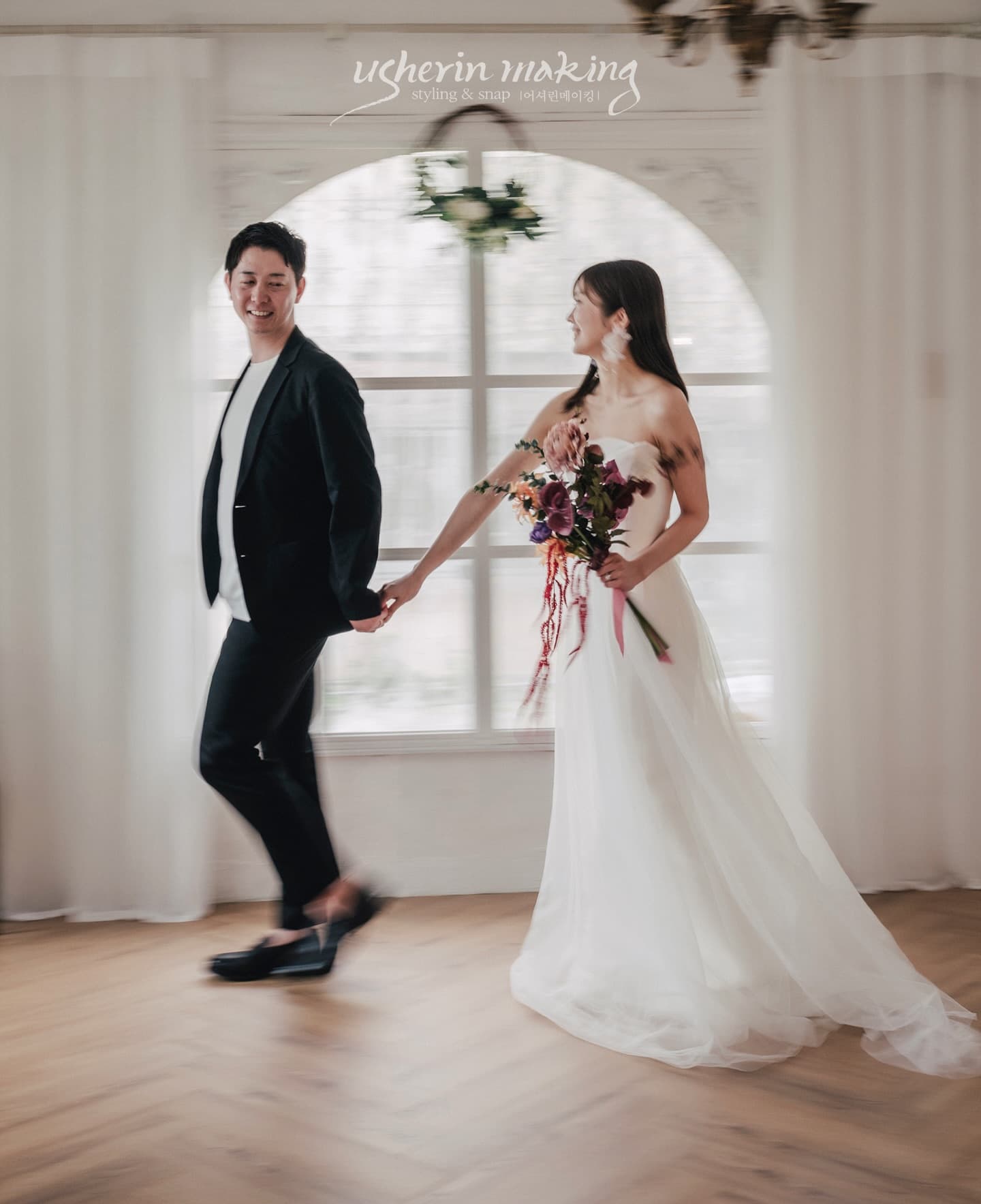 アーチ窓の前を手をつないで歩く新郎新婦、動きのあるスタジオウェディングフォト