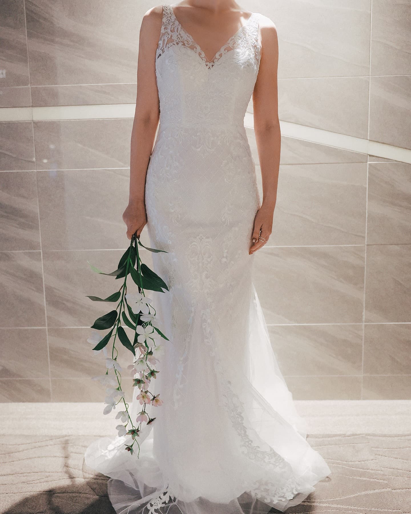 Full-length V-neck sleeveless lace mermaid dress with a tulle overlay, holding a flowering branch
