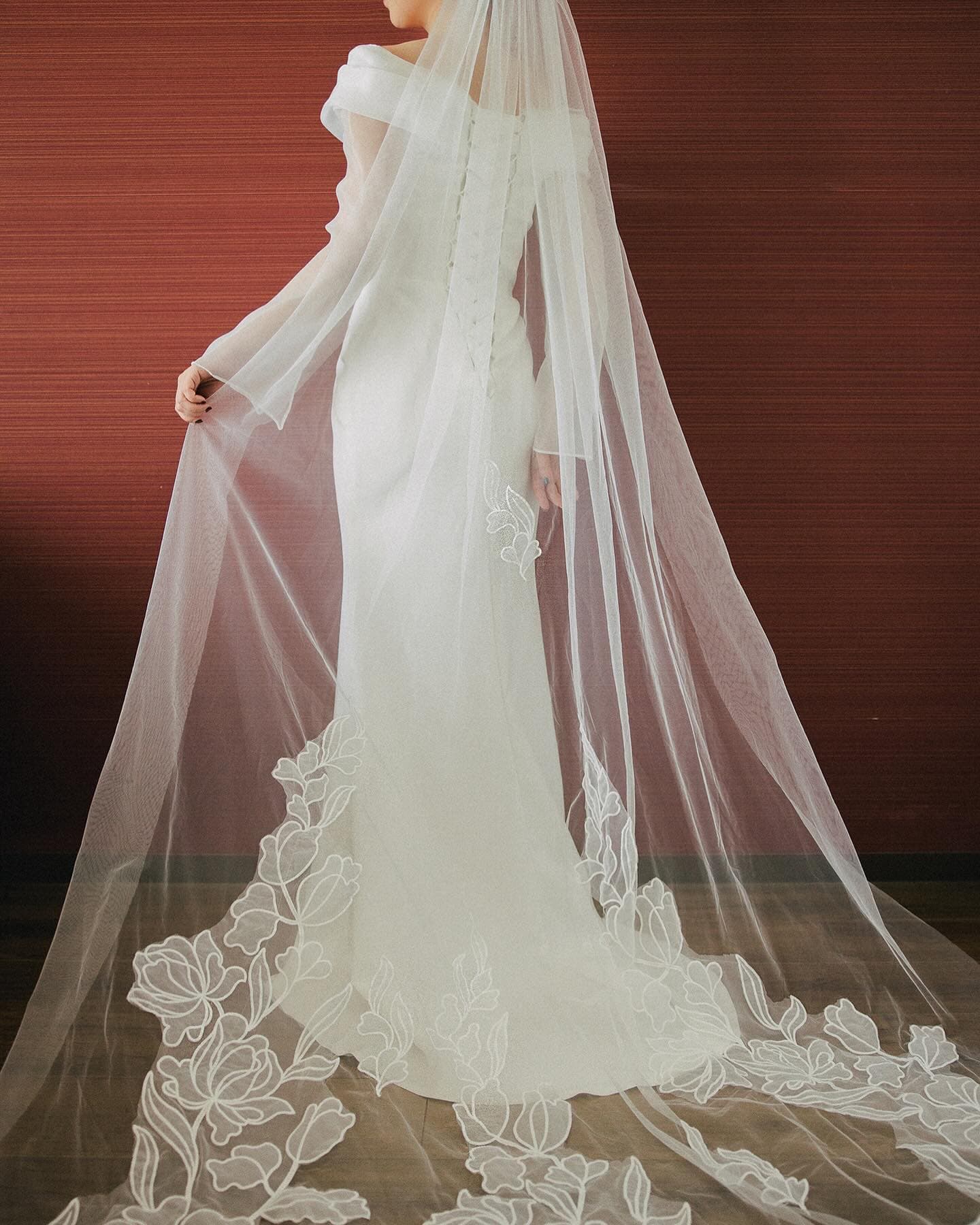 Back view of a long veil with dimensional lace appliqué pooling on the floor