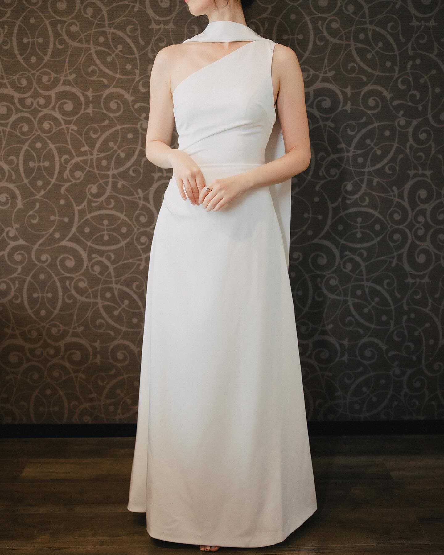 Minimal white gown styled with its long strap draped around the neck, front view