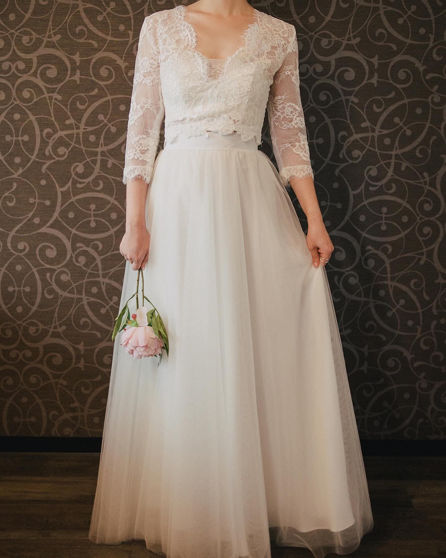 Full-length view of a V-neck lace bolero over a tulle skirt, against patterned wallpaper