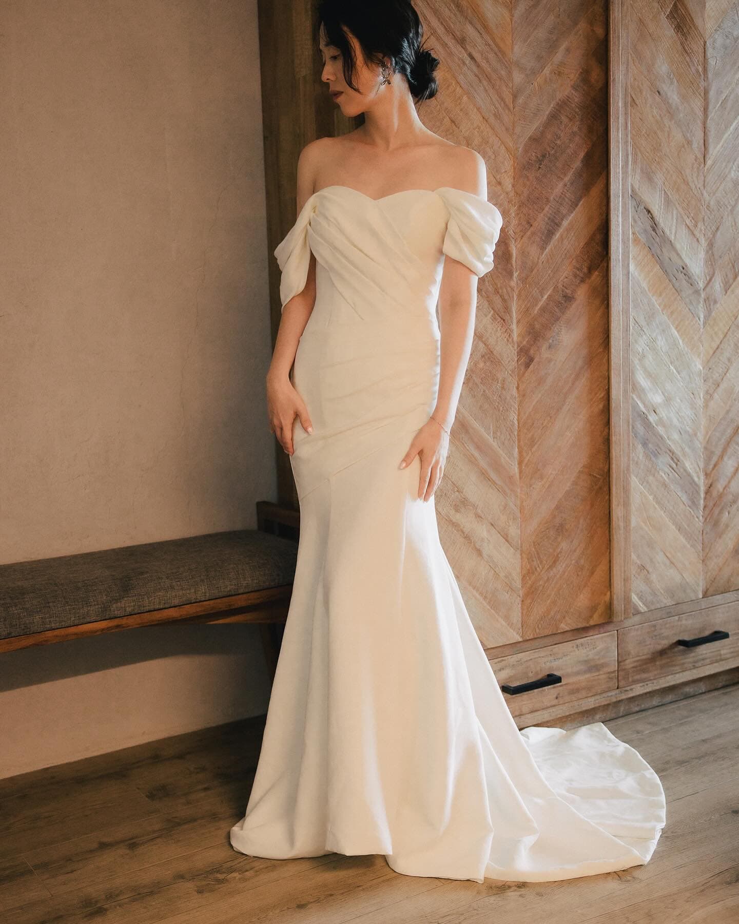 Full-length mermaid dress with draped off-shoulder sleeves in a wood-panelled room