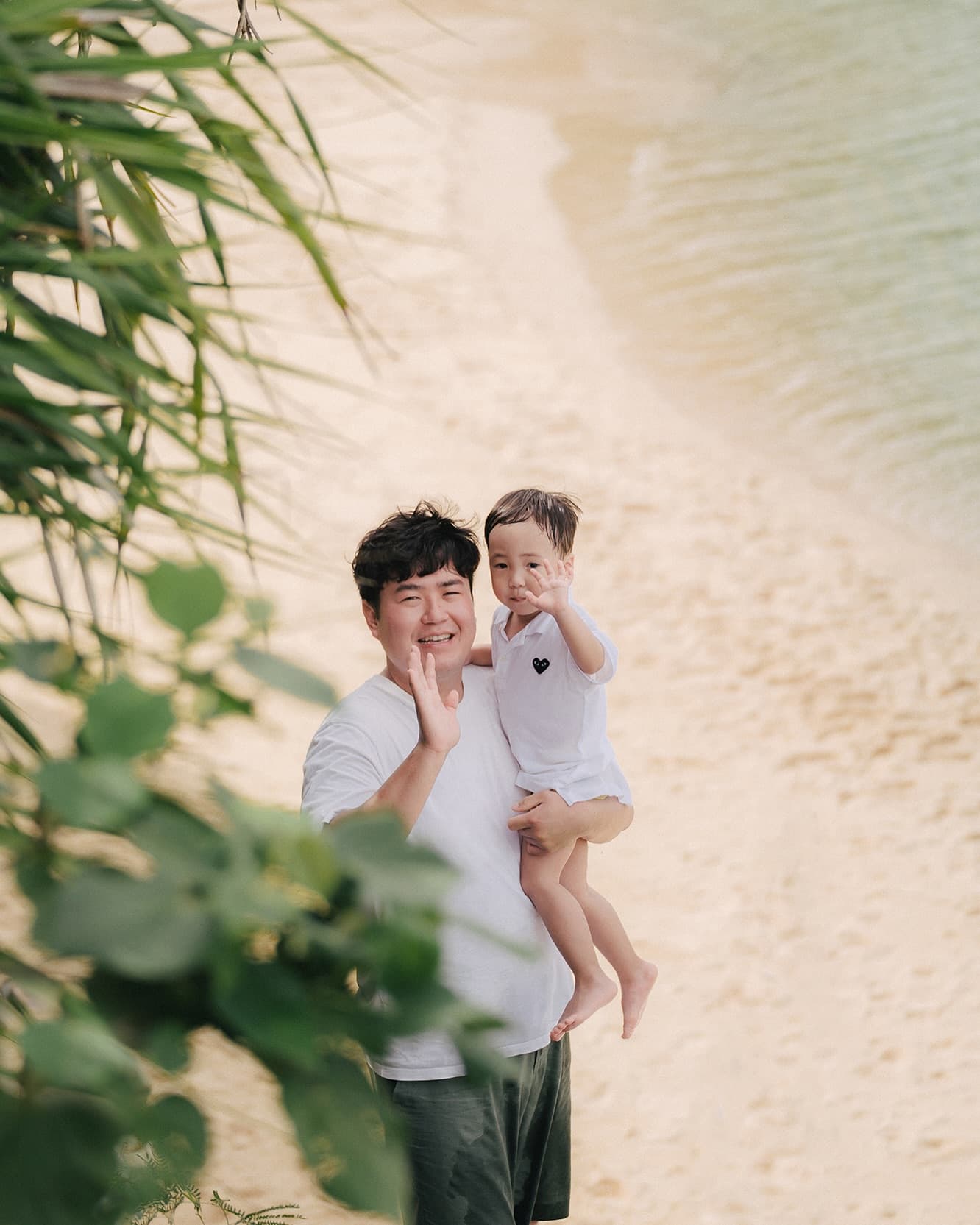 Father holding a waving toddler on a sandy beach in Okinawa