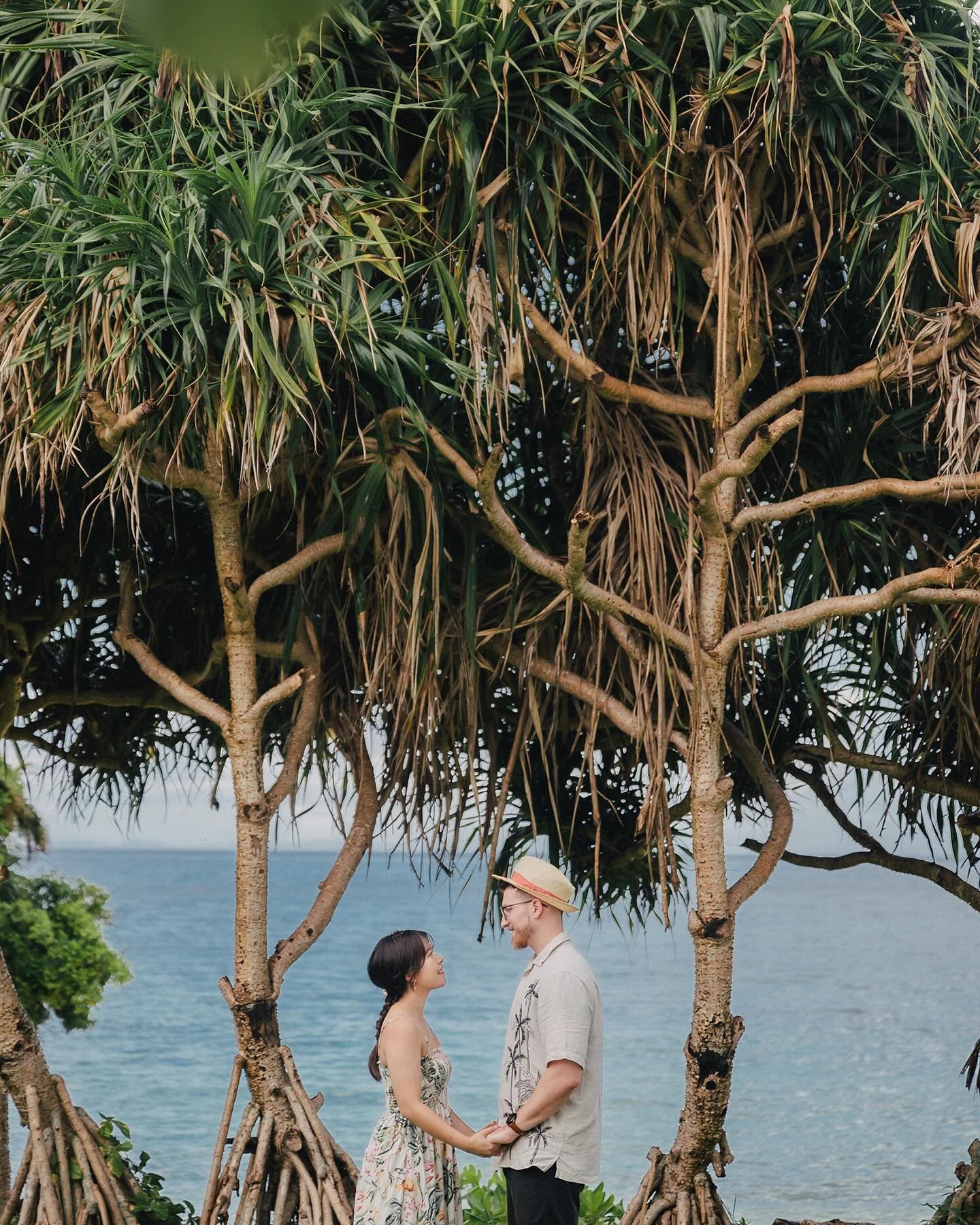 Couple holding hands between pandanus trees by the Okinawa sea